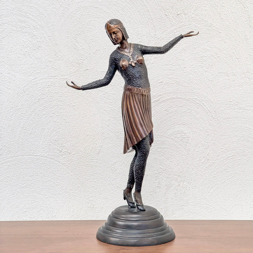 Bronze statue of a woman dancer in vintage attire with extended arms on a round base