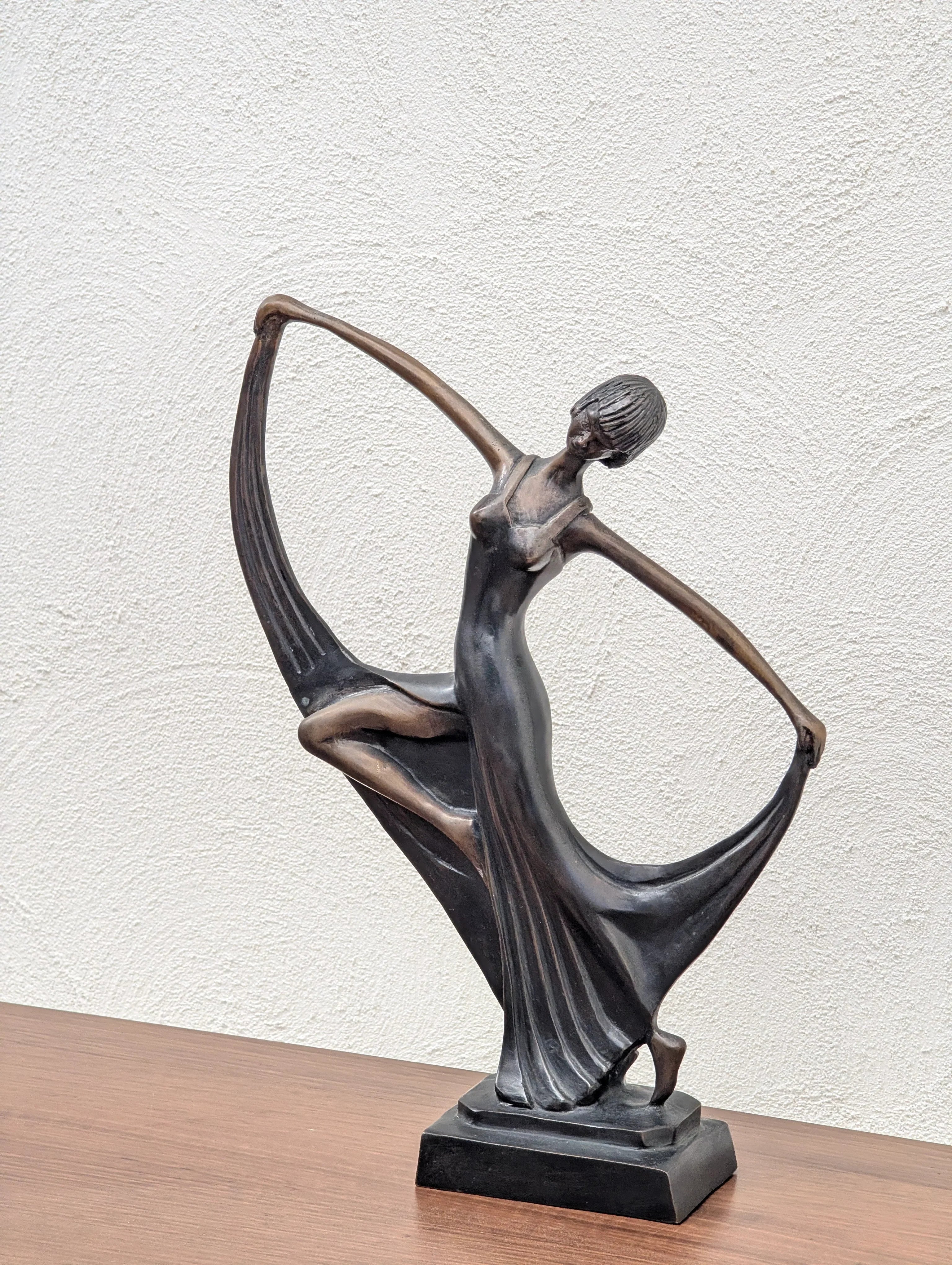 Bronze sculpture of a dancing woman in flowing dress on wooden table against white wall