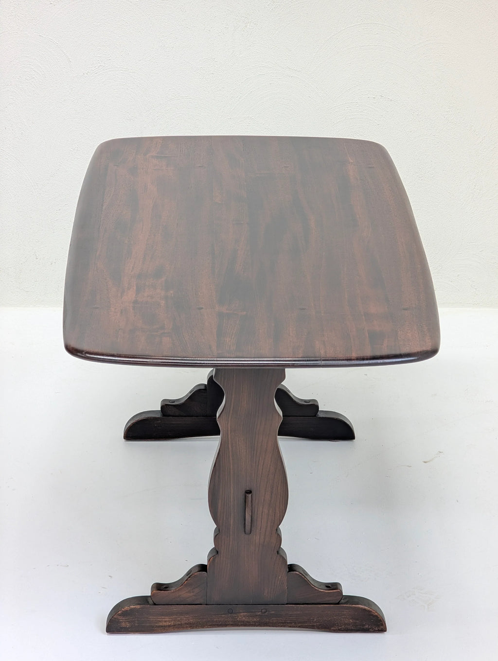 Dark wooden pedestal table with carved base on white floor and light wall background