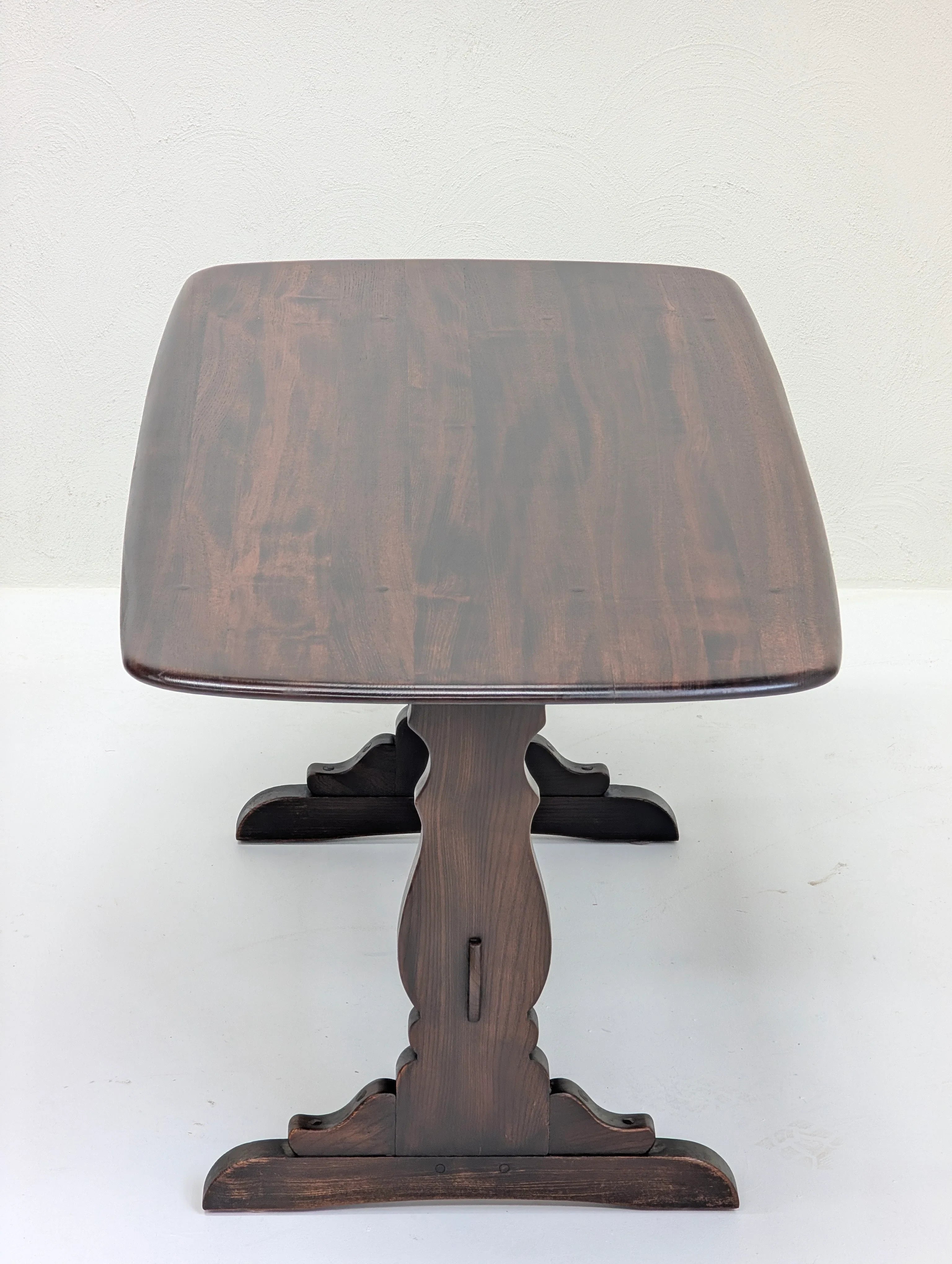 Dark wooden pedestal table with carved base on white floor and light wall background