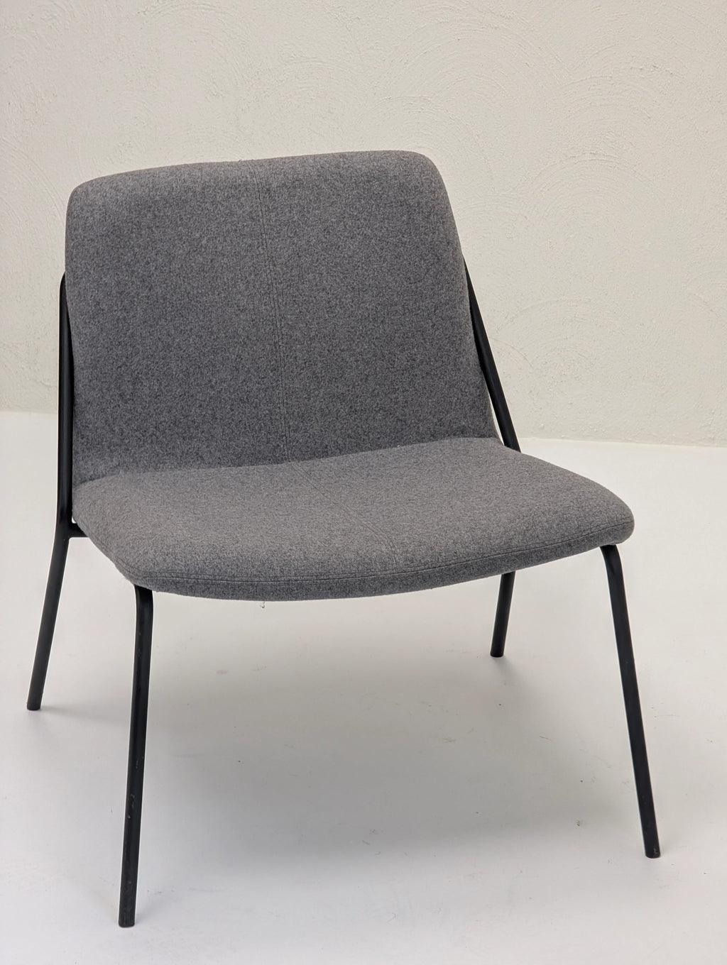 Modern grey fabric lounge chair with black metal legs on white floor and textured wall