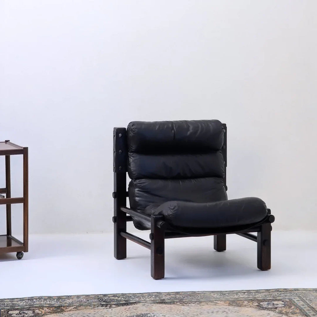 Mid-century modern black leather lounge chair with dark wood frame in minimalist room