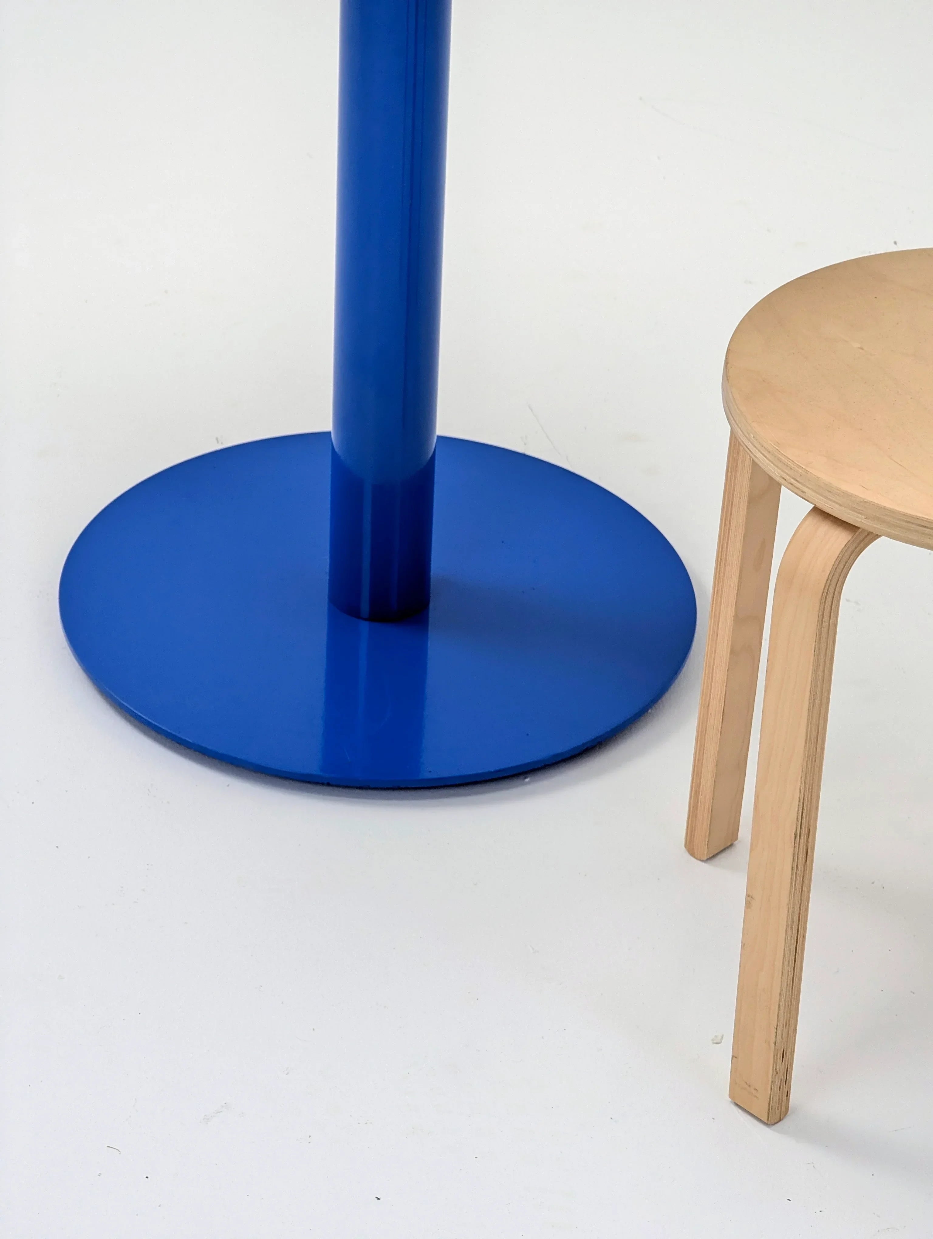 Blue metal table base beside a light wood stool on white background