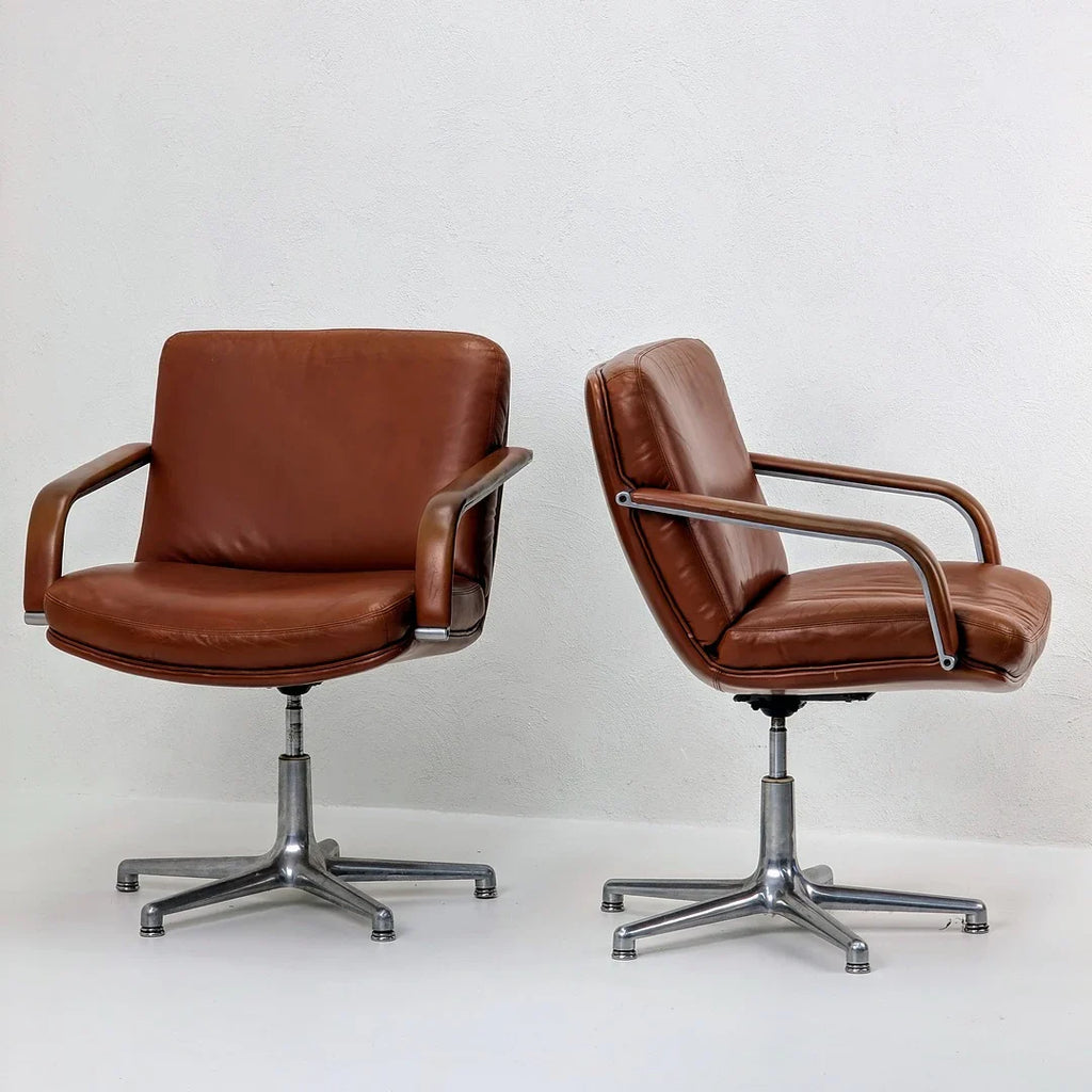 Pair of vintage brown leather swivel chairs with chrome bases against a white wall