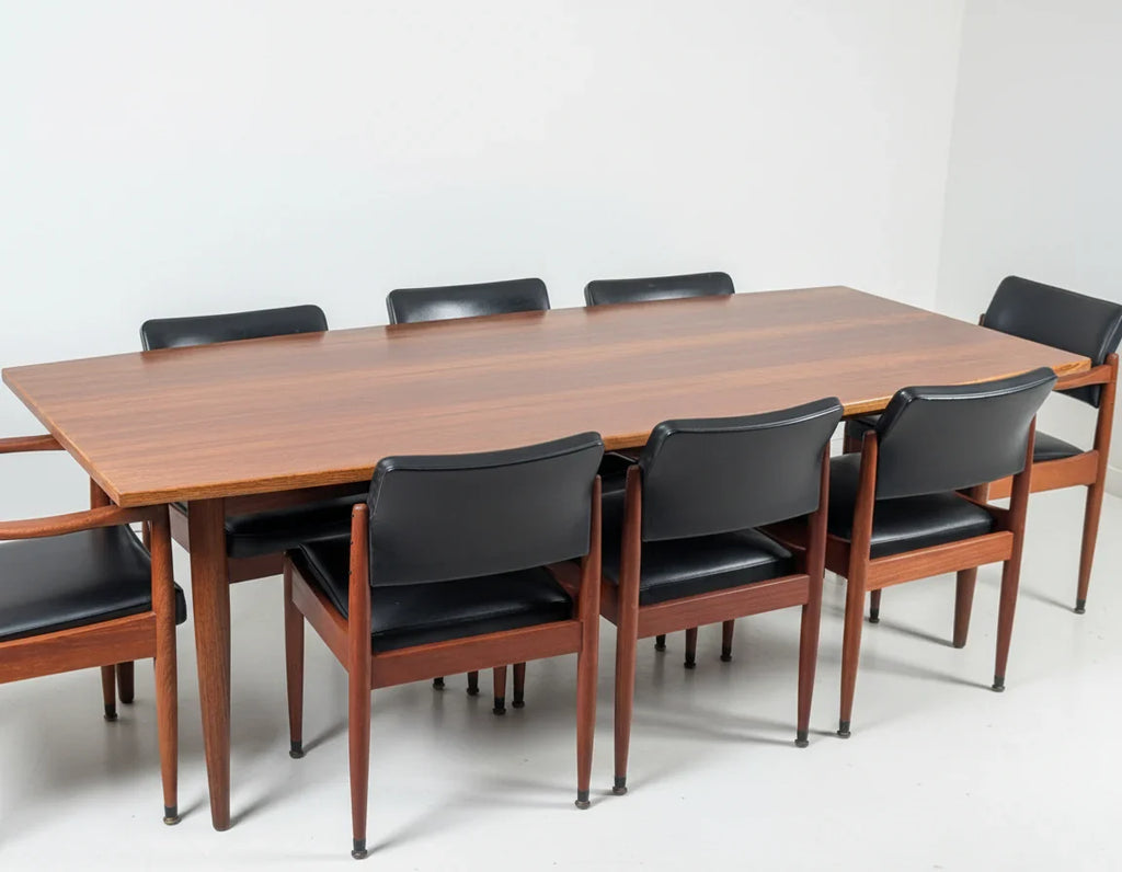 Mid-century modern wooden dining table with eight black leather and teak chairs in minimalist setting