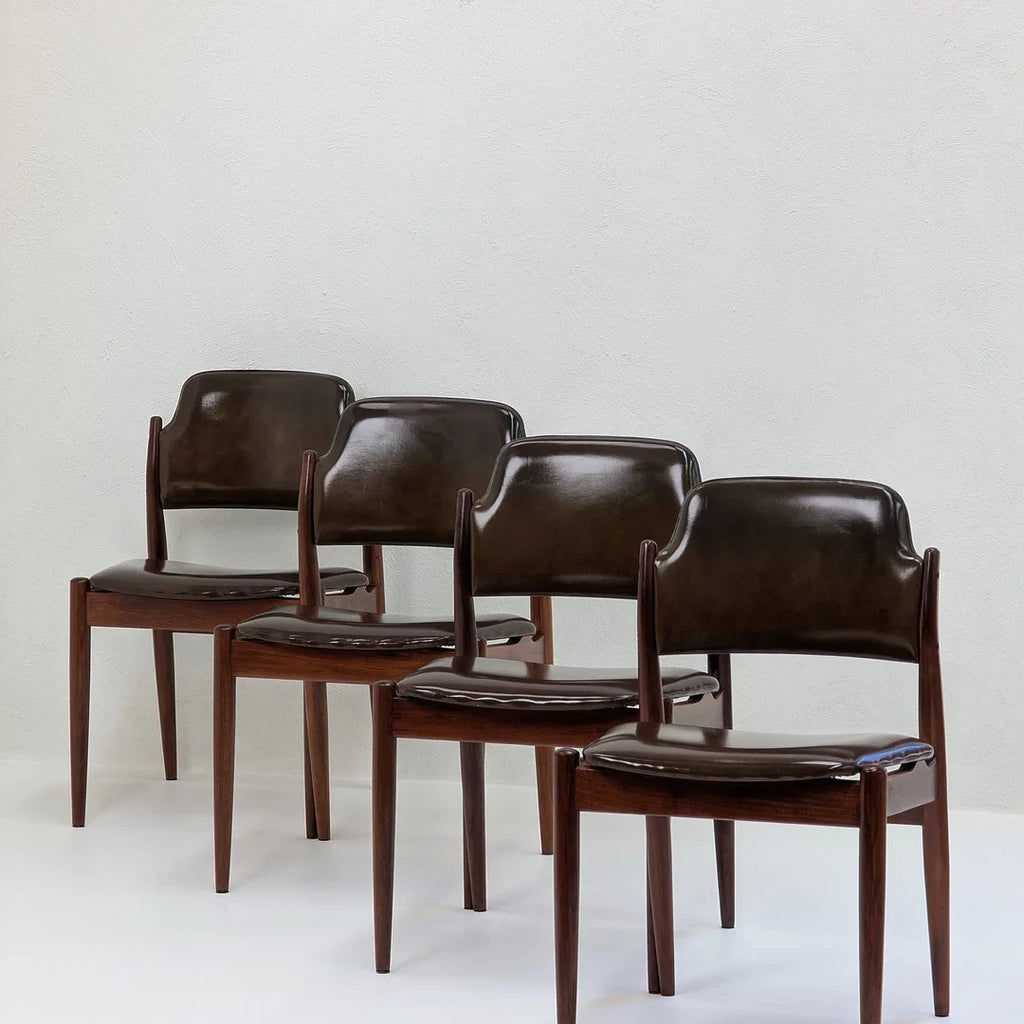 Set of four vintage brown leather dining chairs with wooden legs against a white wall