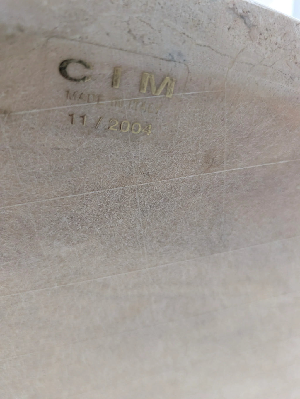 Close-up of textured surface stamped with CIM Made in Italy 11/2004 in gold lettering.