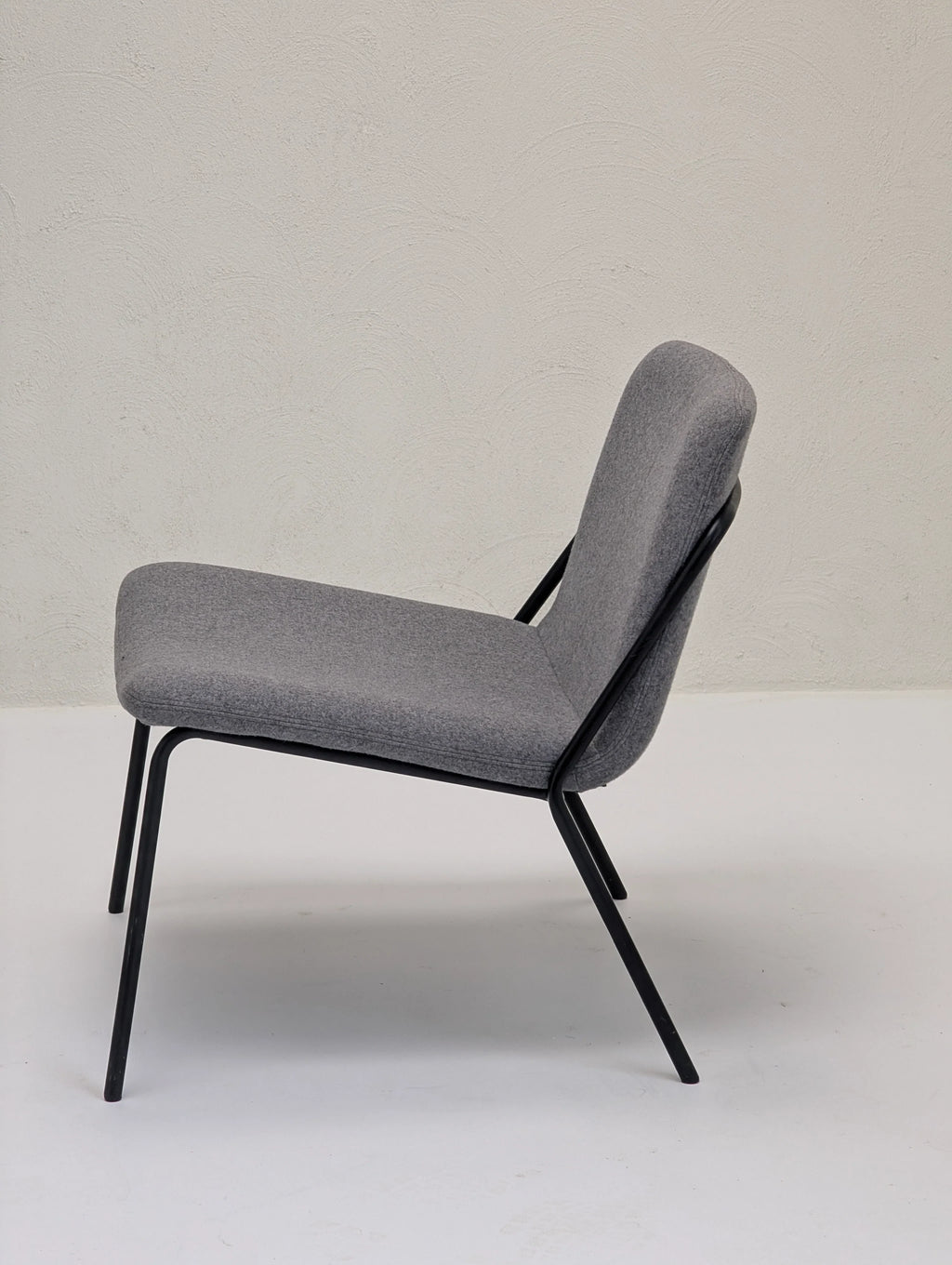 Modern gray upholstered lounge chair with black metal legs against textured beige wall