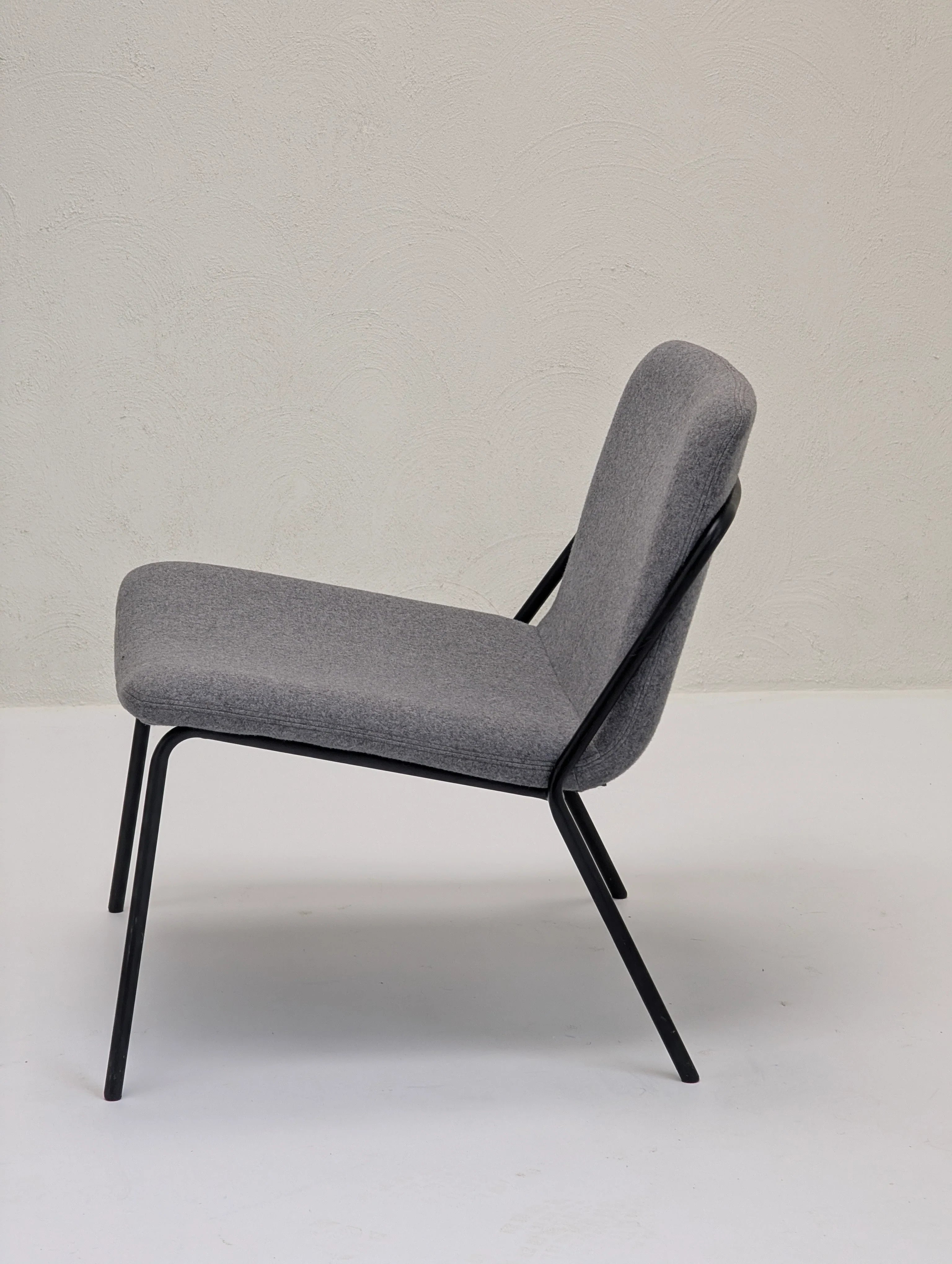 Modern gray upholstered lounge chair with black metal legs against textured beige wall