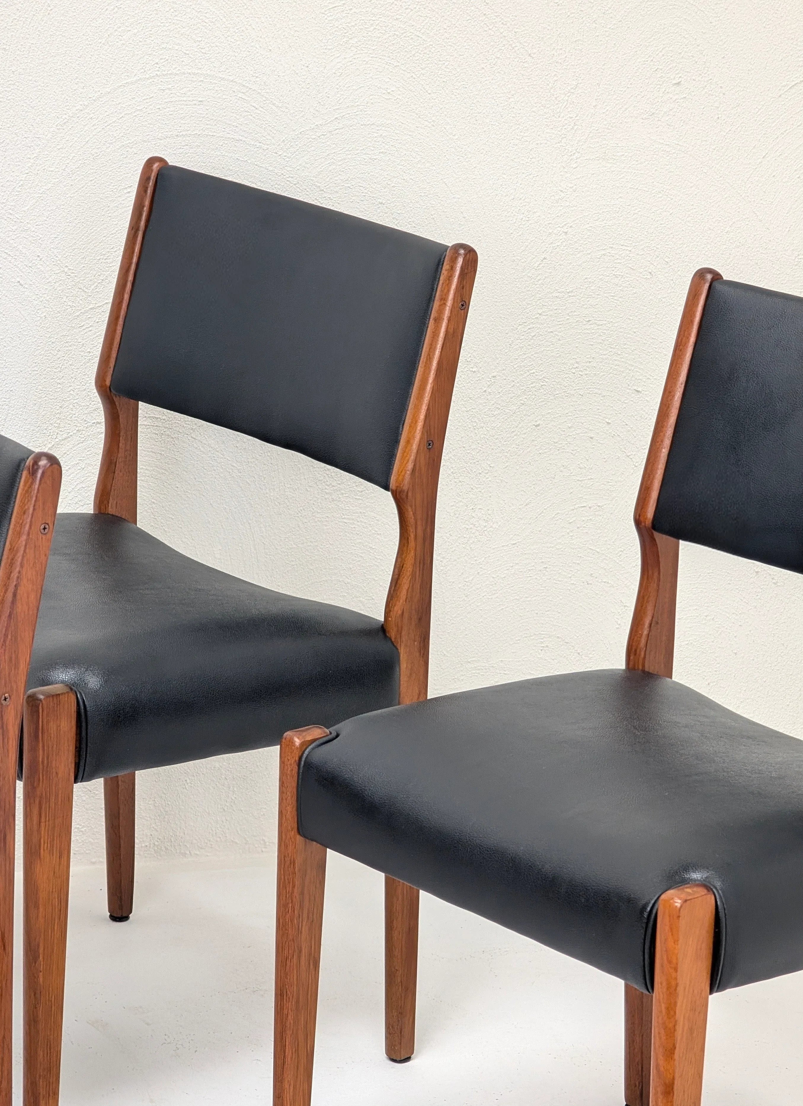 Two mid-century modern wooden chairs with black leather seats and backs against a textured white wall