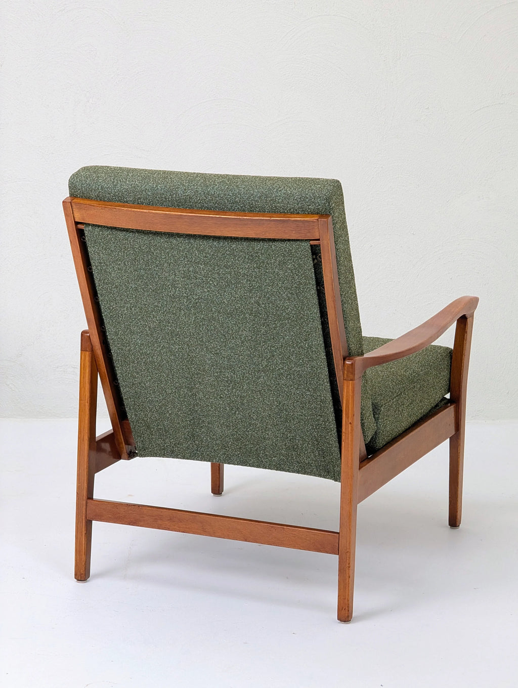Mid-century modern wooden armchair with green upholstered back and seat against white wall
