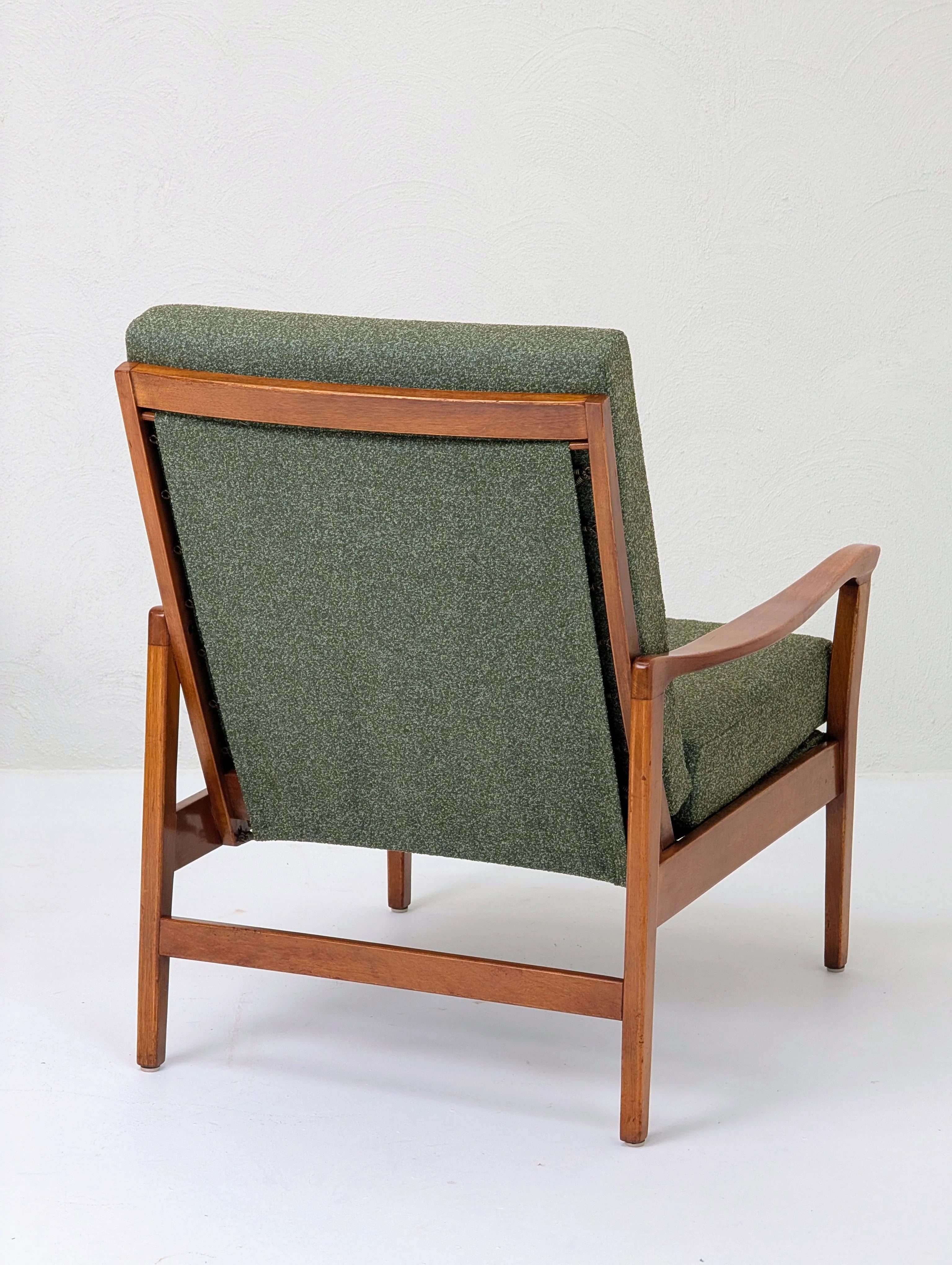 Mid-century modern wooden armchair with green upholstered back and seat against white wall