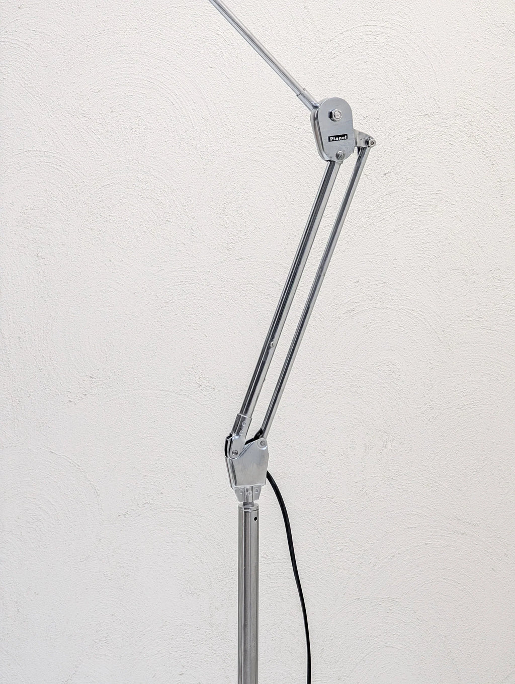 Chrome adjustable desk lamp arm by Planet against a textured white wall