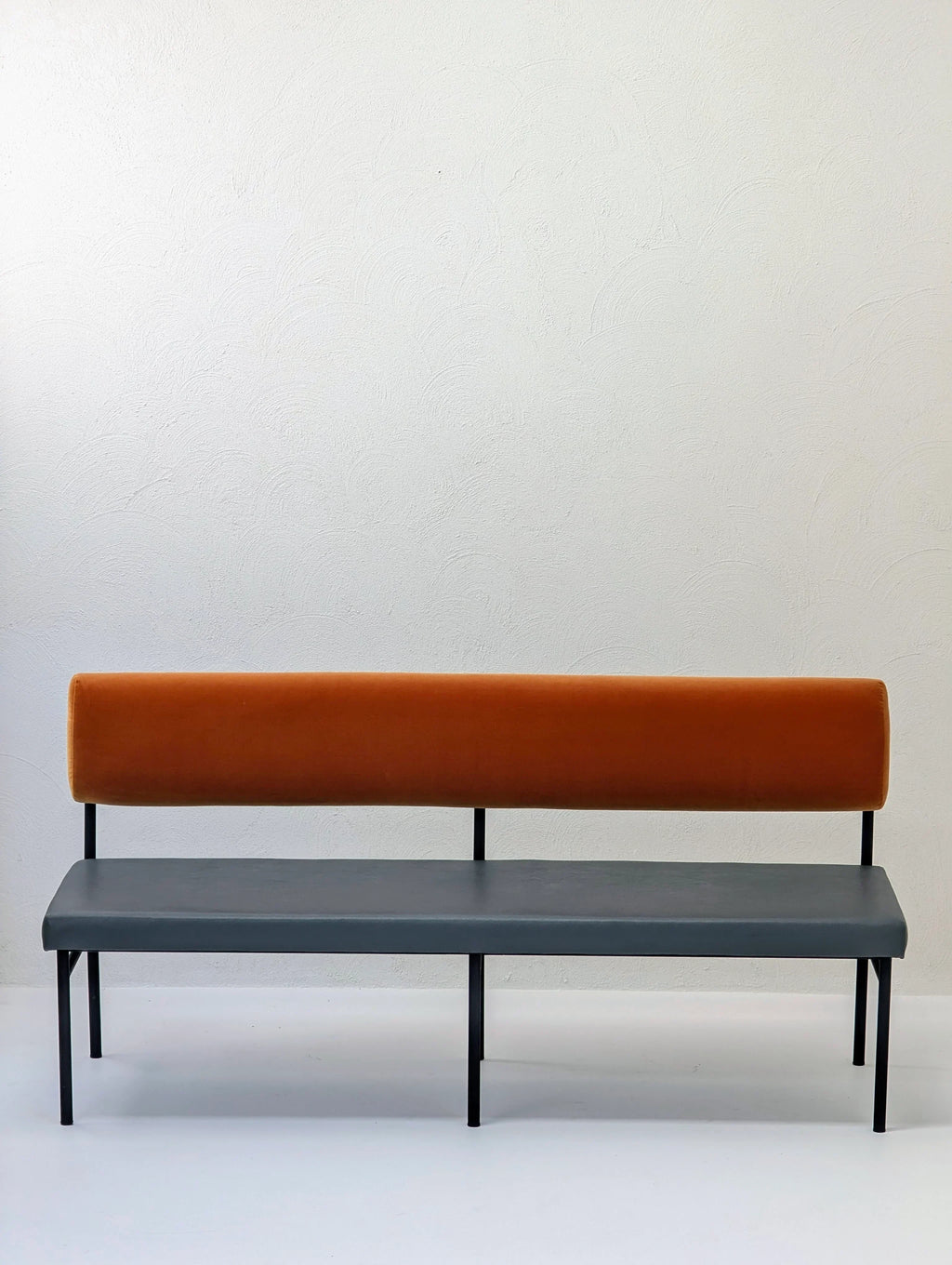 Modern bench with orange backrest and gray seat against a plain white wall
