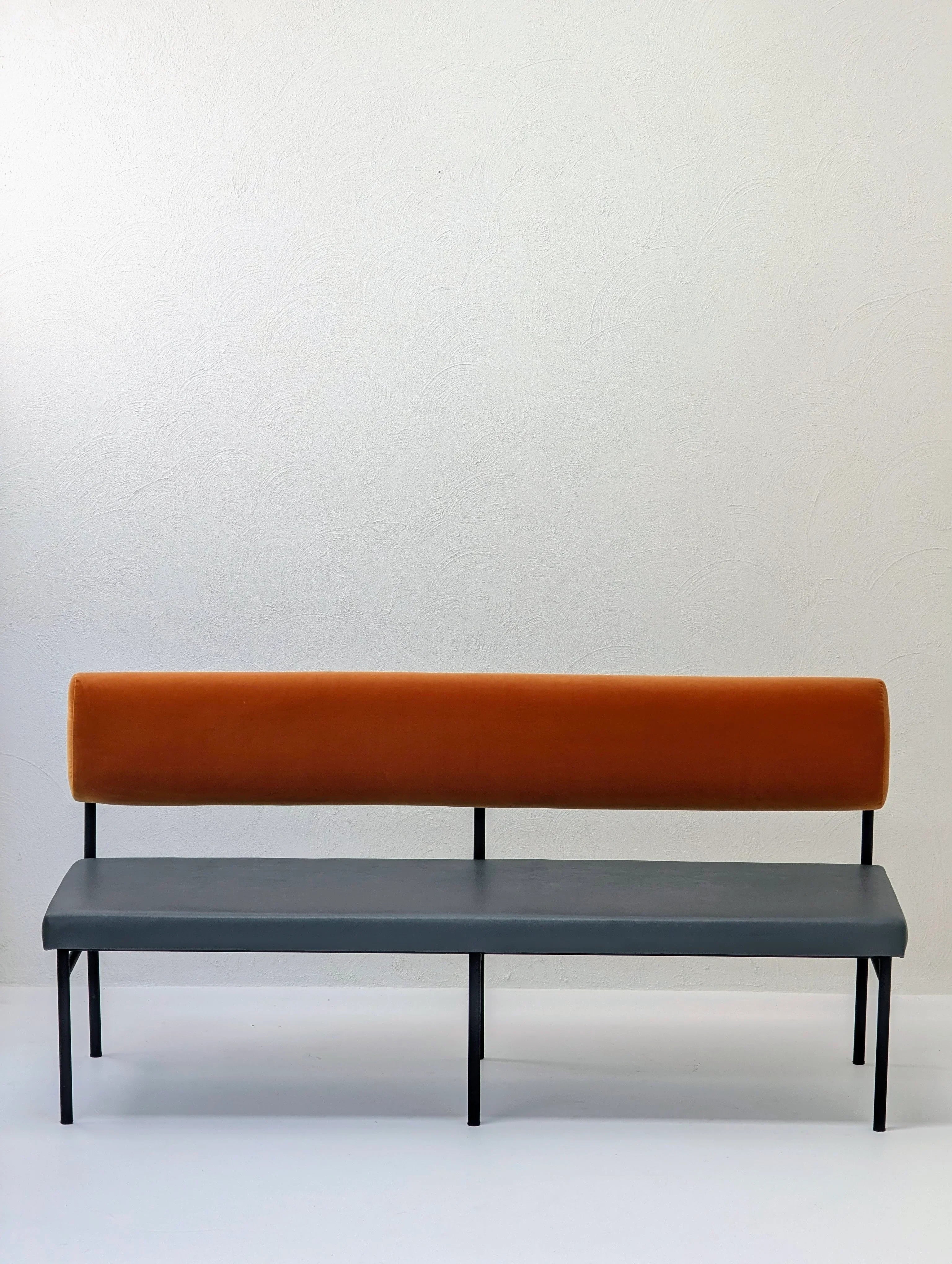 Modern bench with orange backrest and gray seat against a plain white wall