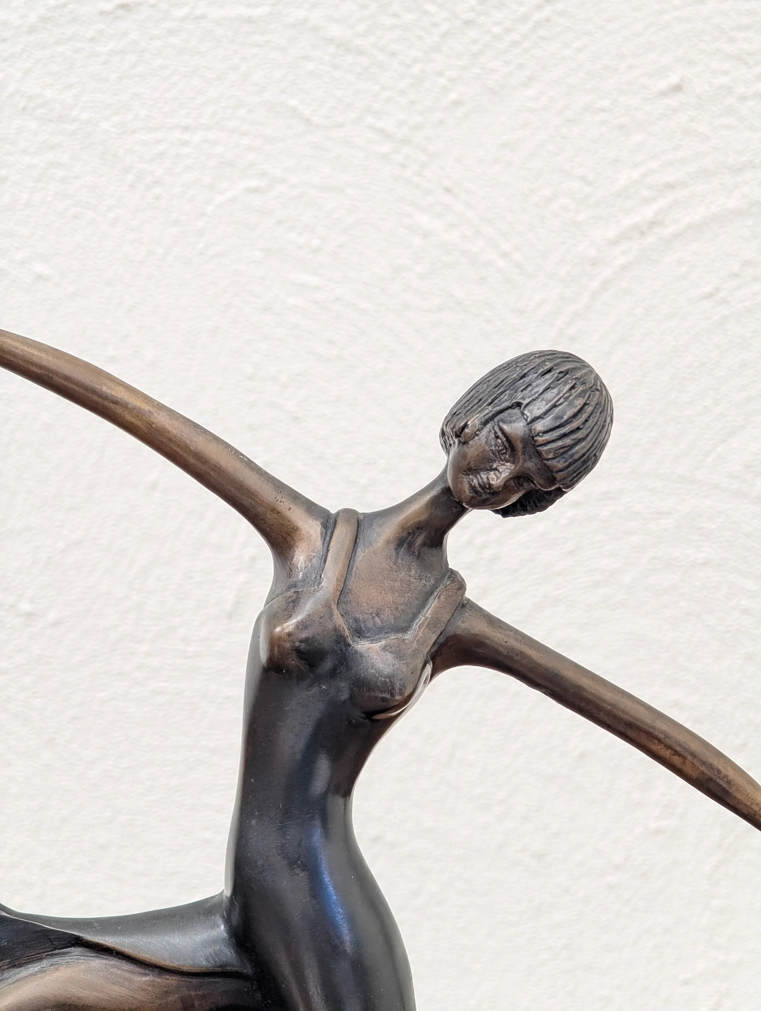 Bronze sculpture of a female dancer with outstretched arms and short hair against a white textured background