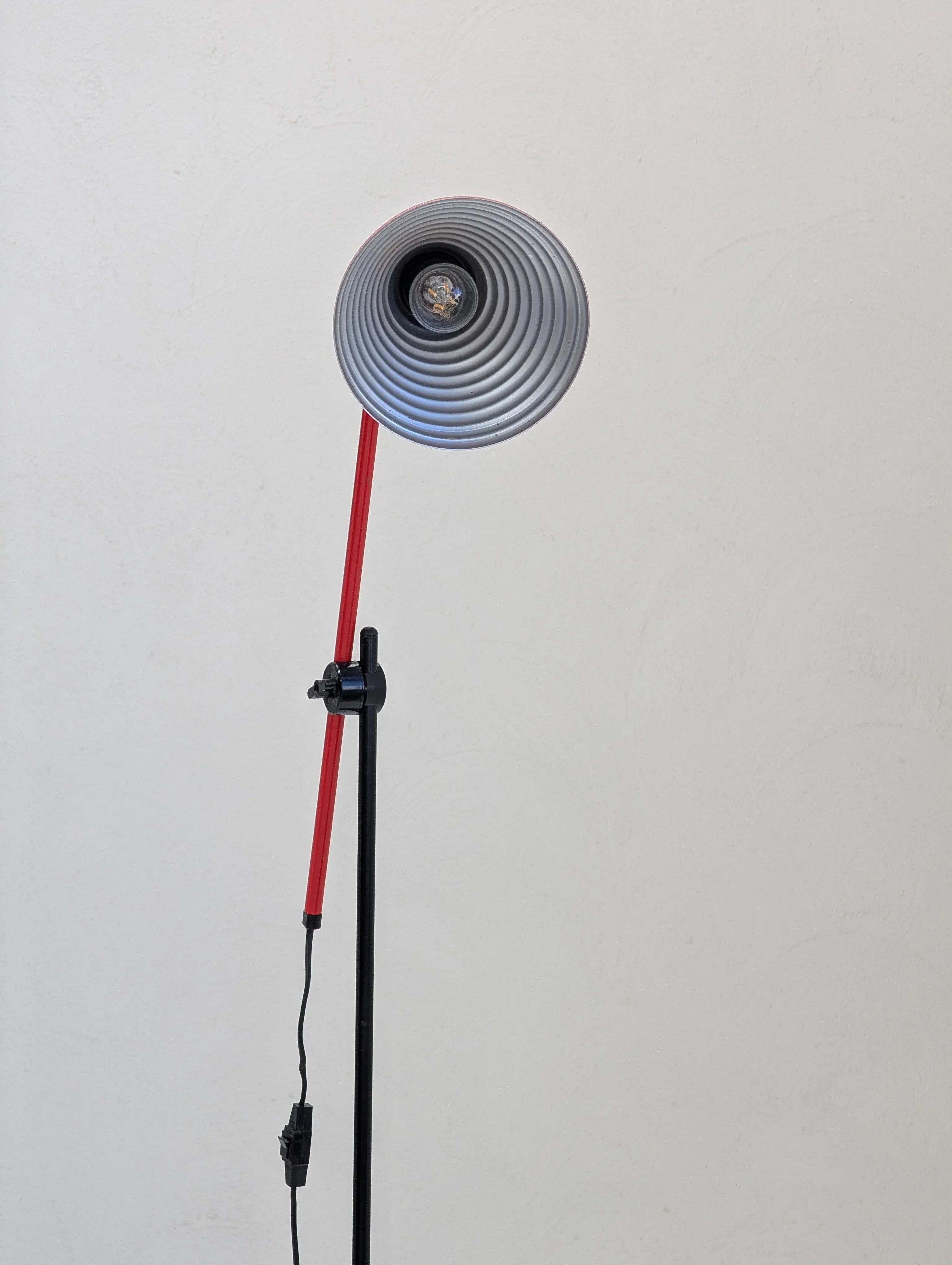 Modern studio lamp with a red stand and circular gray shade against a plain white wall