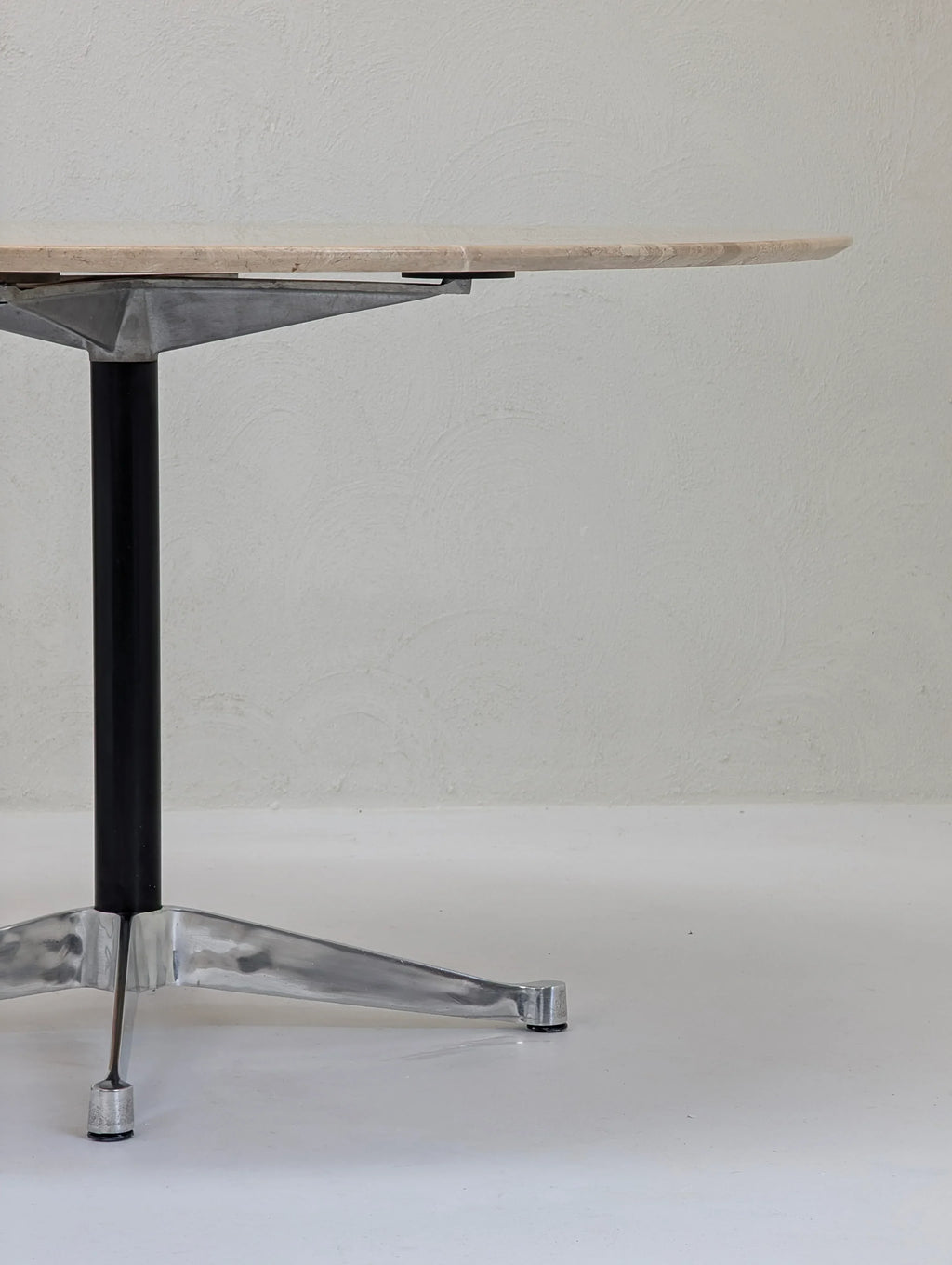 Round wood table with metal pedestal base and tripod legs against a light textured wall
