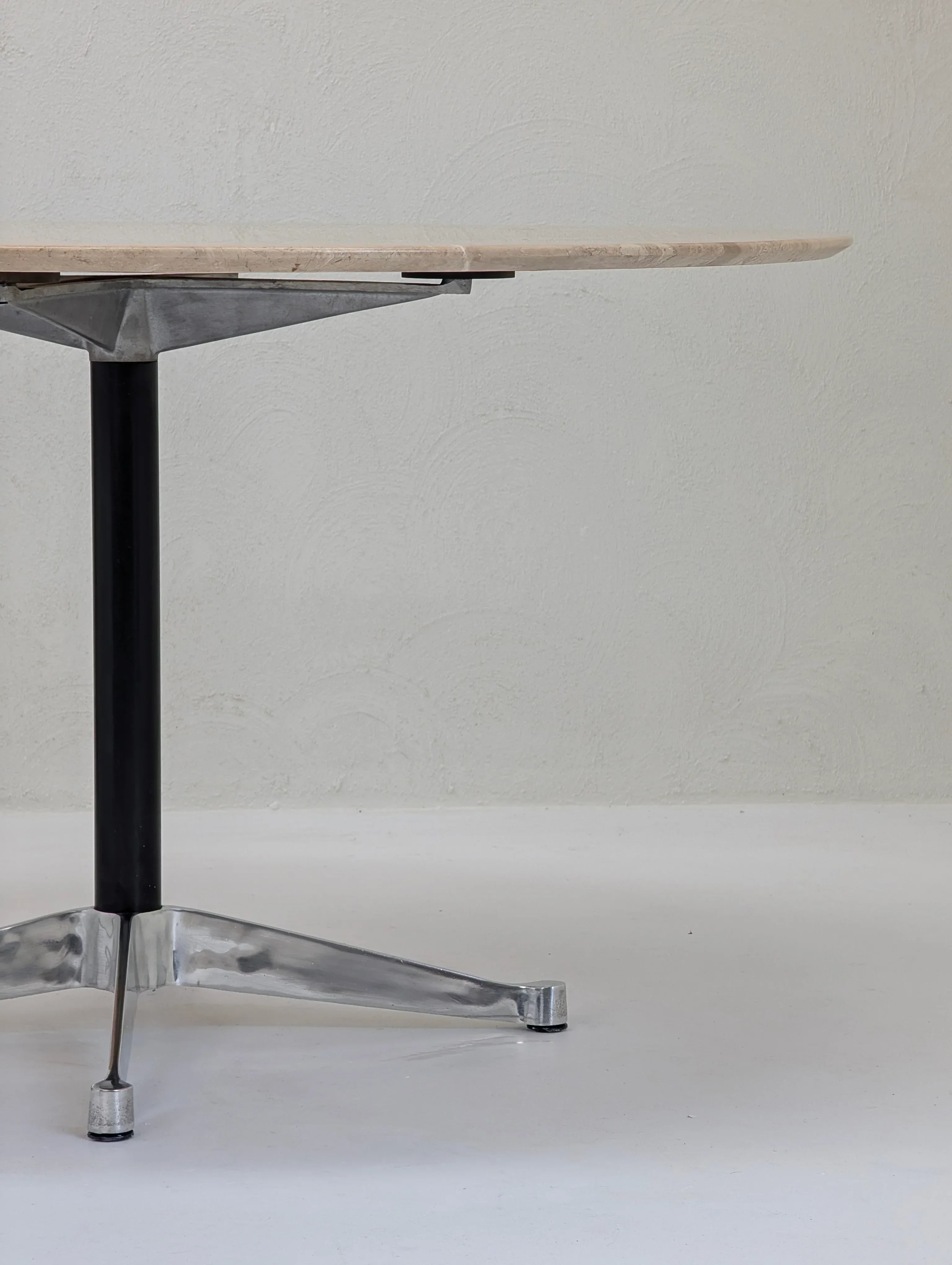 Round wood table with metal pedestal base and tripod legs against a light textured wall