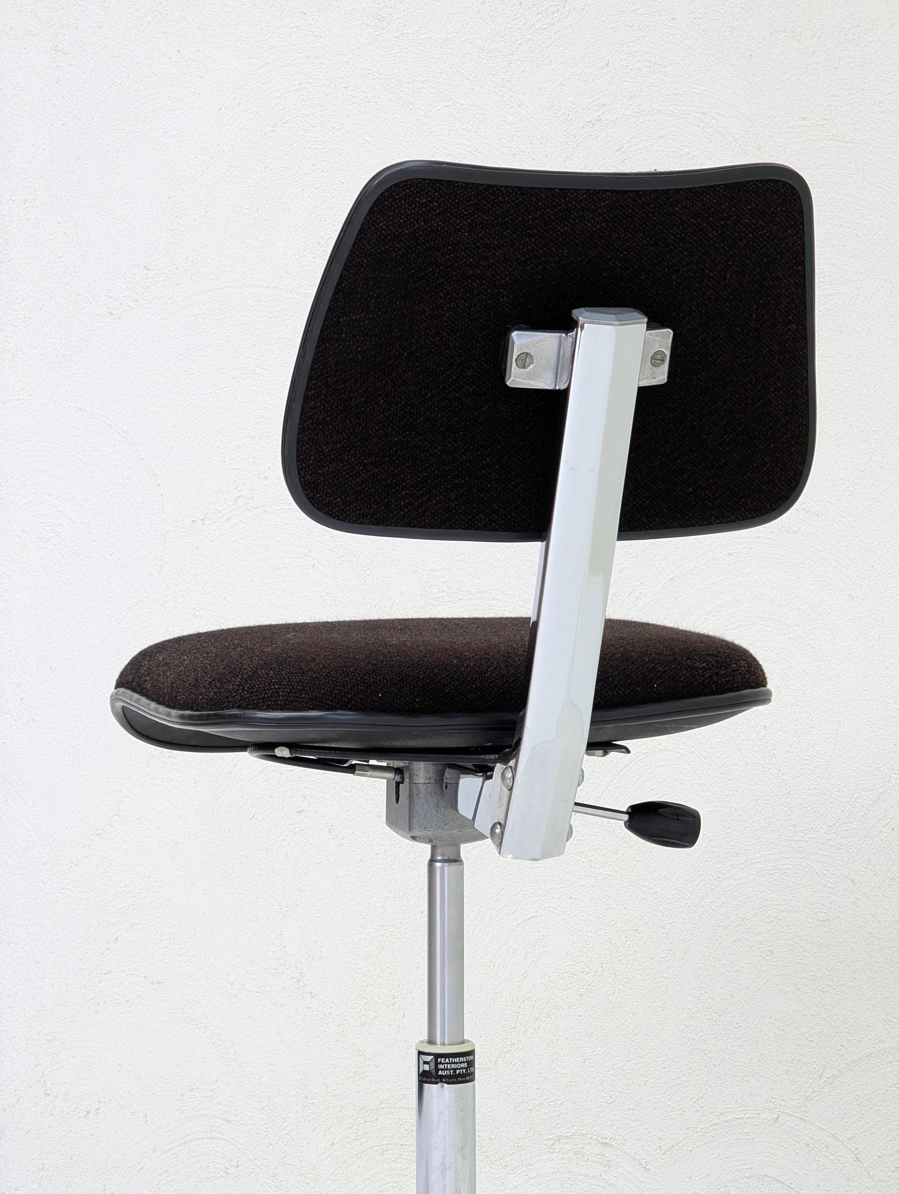 Black cushioned office chair with chrome metal frame and adjustable height lever against white wall
