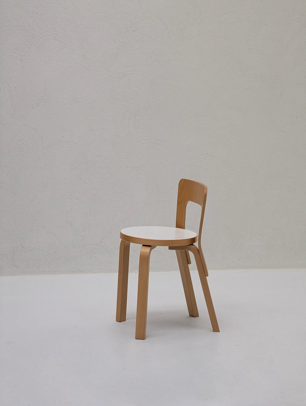 Minimalist wooden chair with white seat in a bright, modern room with textured wall
