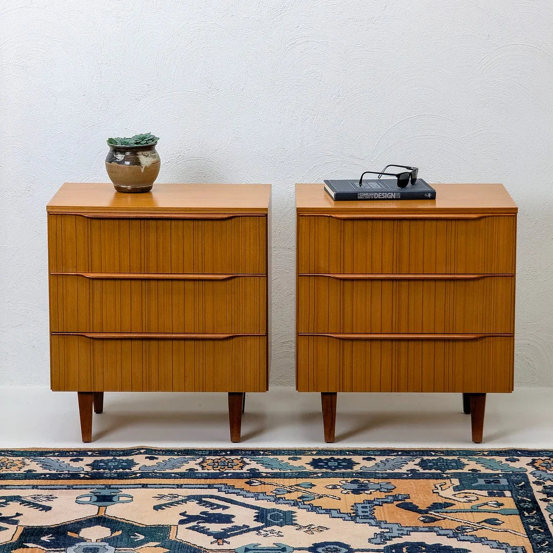 Pair of mid-century modern wooden dressers with a plant, book, and glasses on top, on patterned rug.