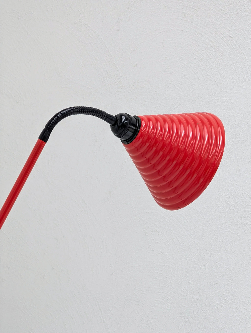Red modern desk lamp with spiral shade against a white textured wall