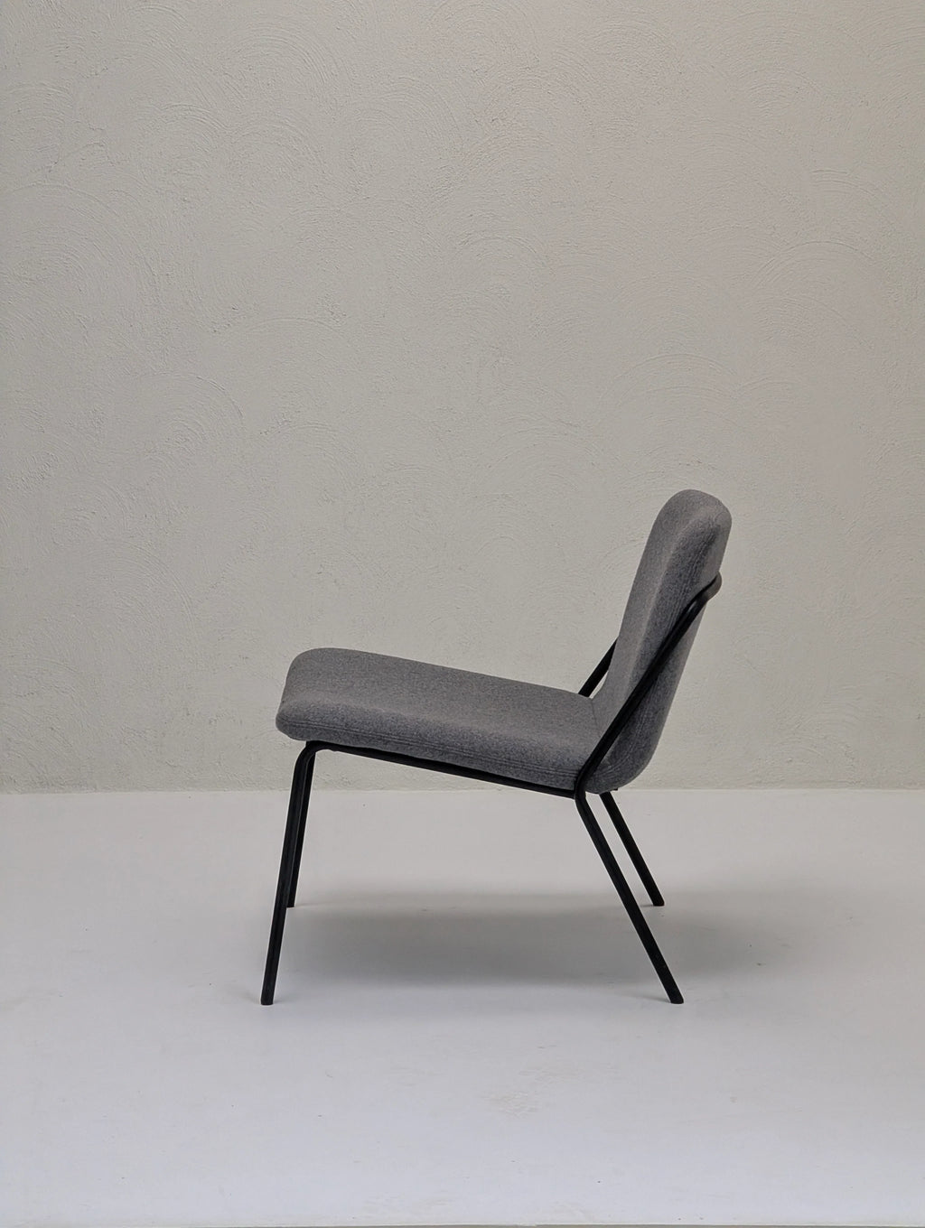 Modern grey upholstered chair with black metal legs on plain white floor and textured light wall
