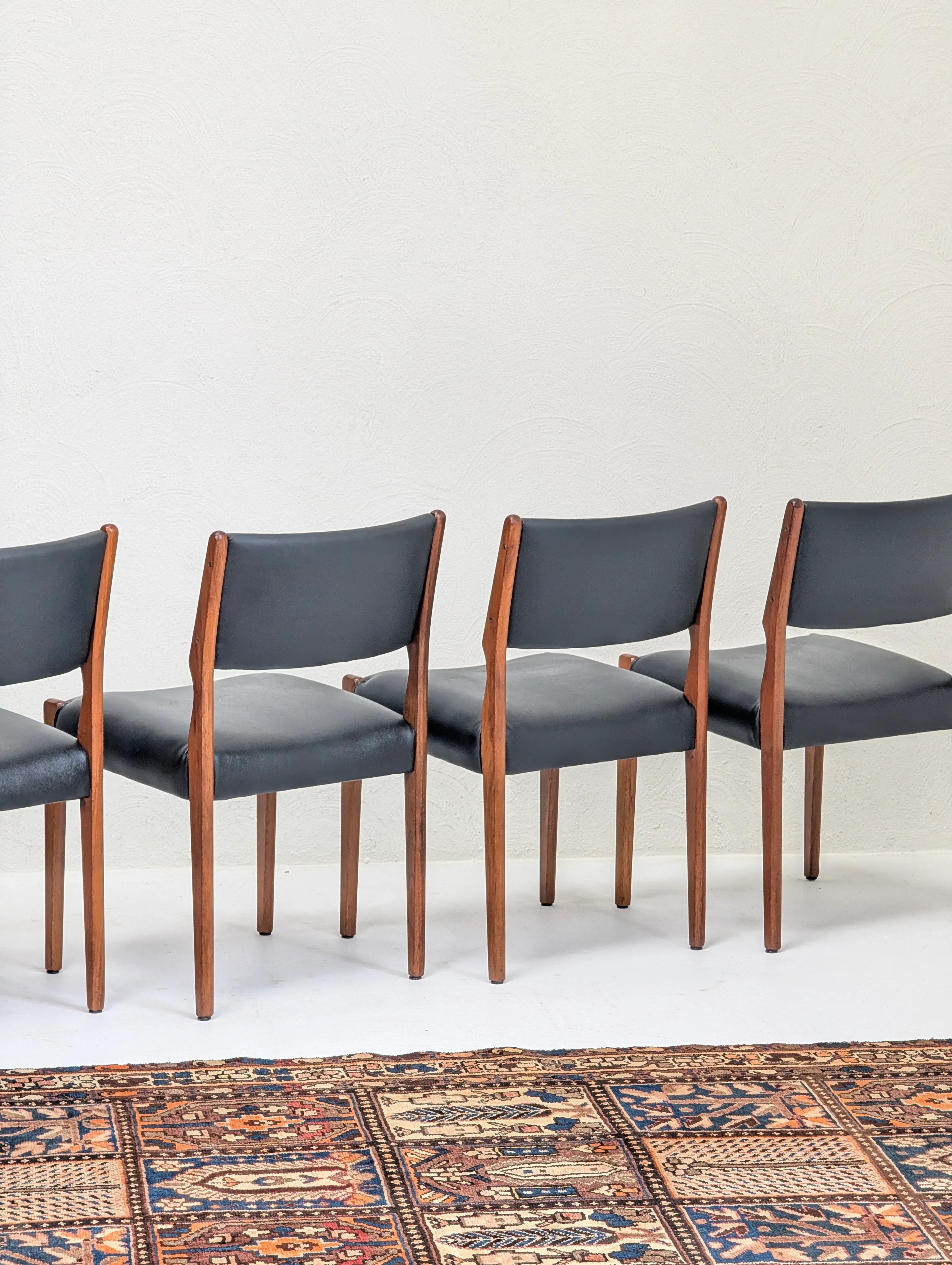 Four mid-century modern chairs with black leather seats and wooden frames on a patterned rug