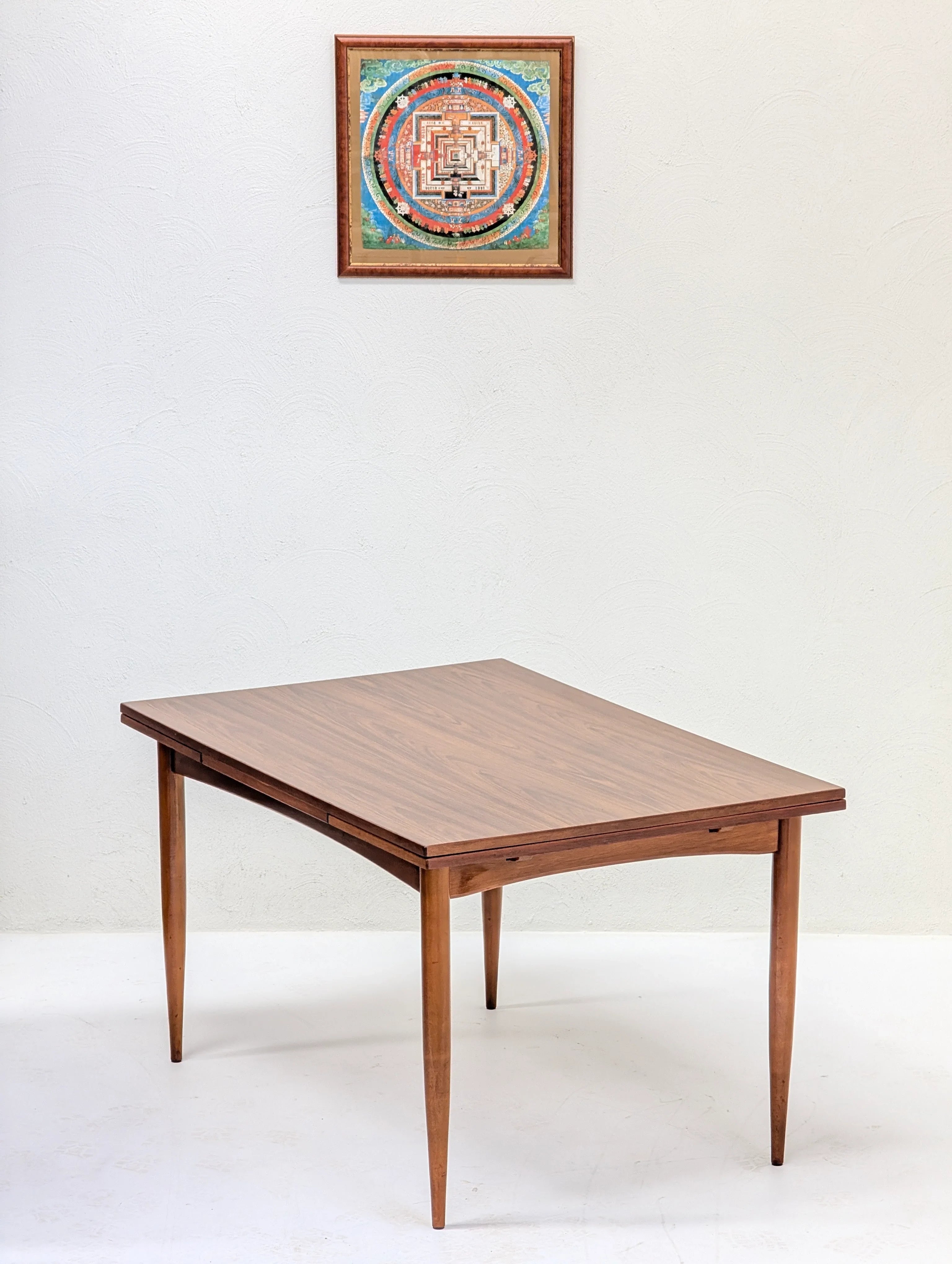 Minimalist wooden dining table with tapered legs against a white wall with framed colorful geometric artwork