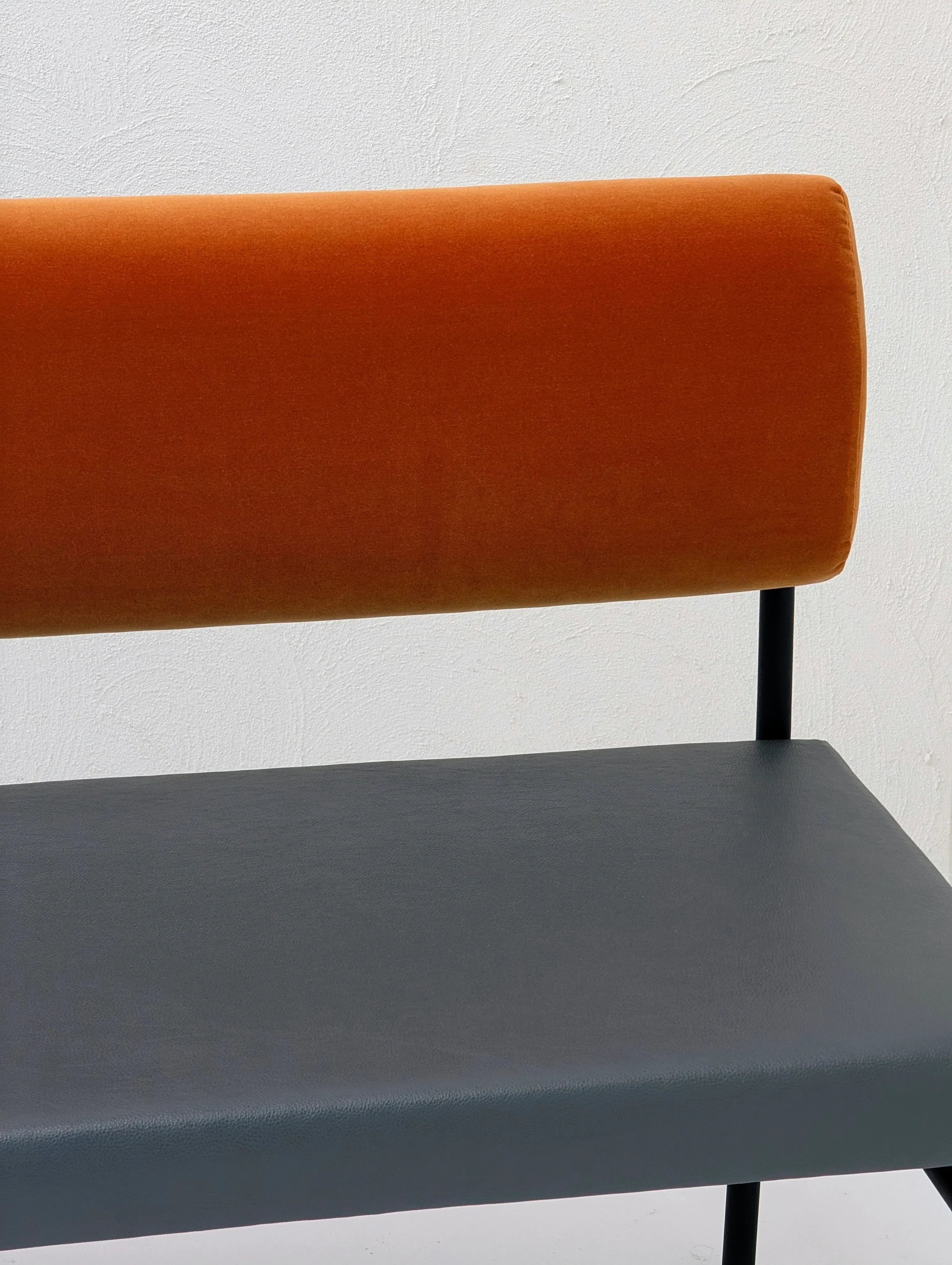 Modern bench with orange velvet backrest and dark gray leather seat against a white wall
