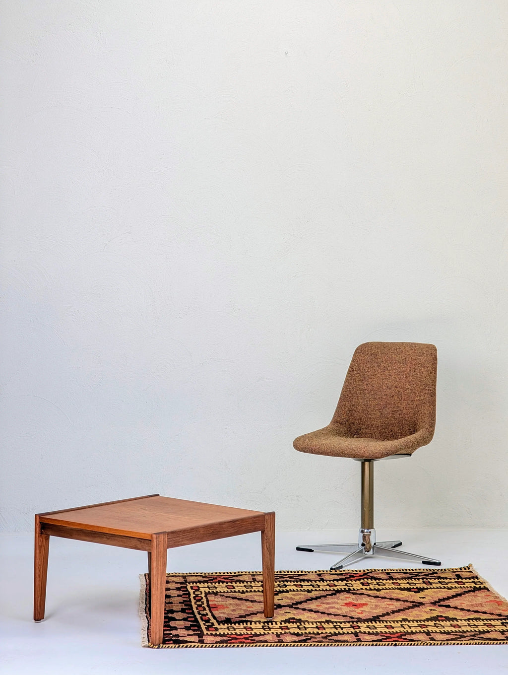 Modern brown swivel chair, wooden square coffee table, and patterned rug against white textured wall