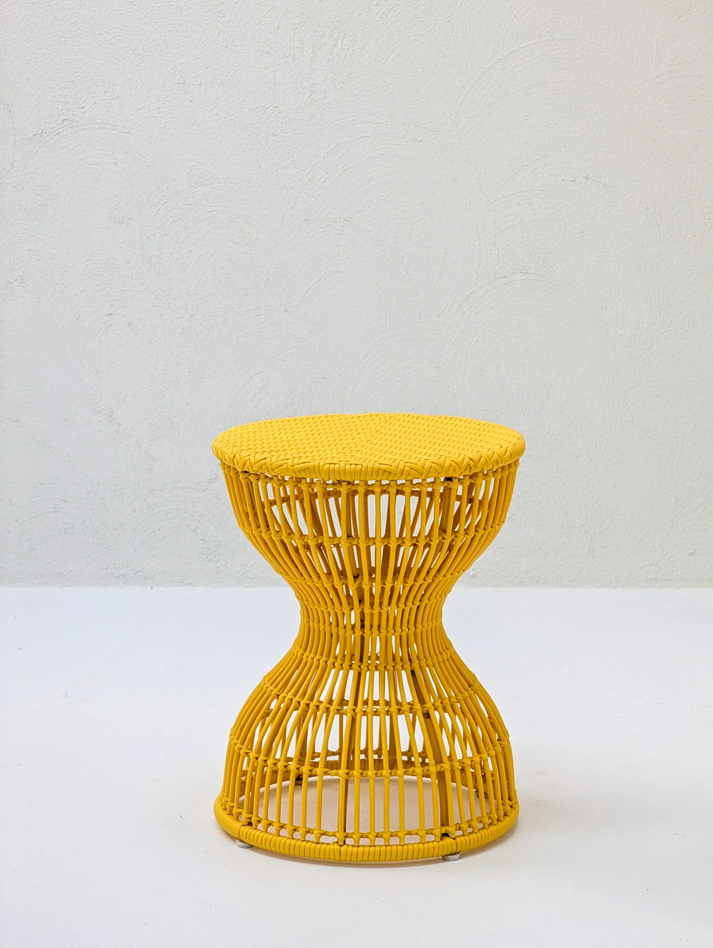 Yellow rattan hourglass stool on white background, modern woven furniture
