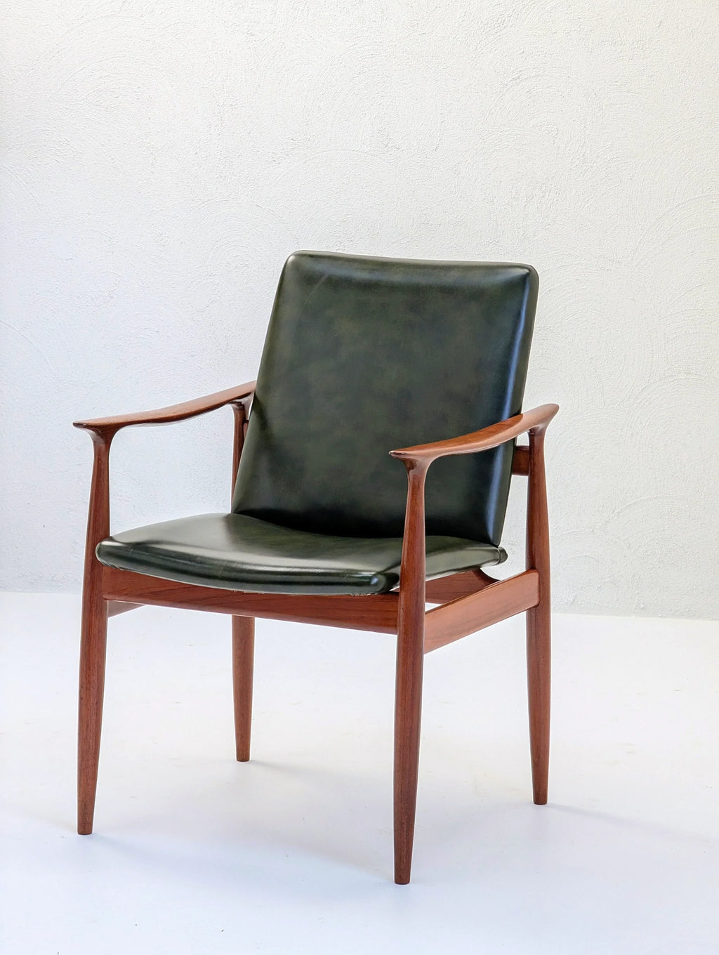 Mid-century modern armchair with green leather upholstery and teak wood frame against white wall