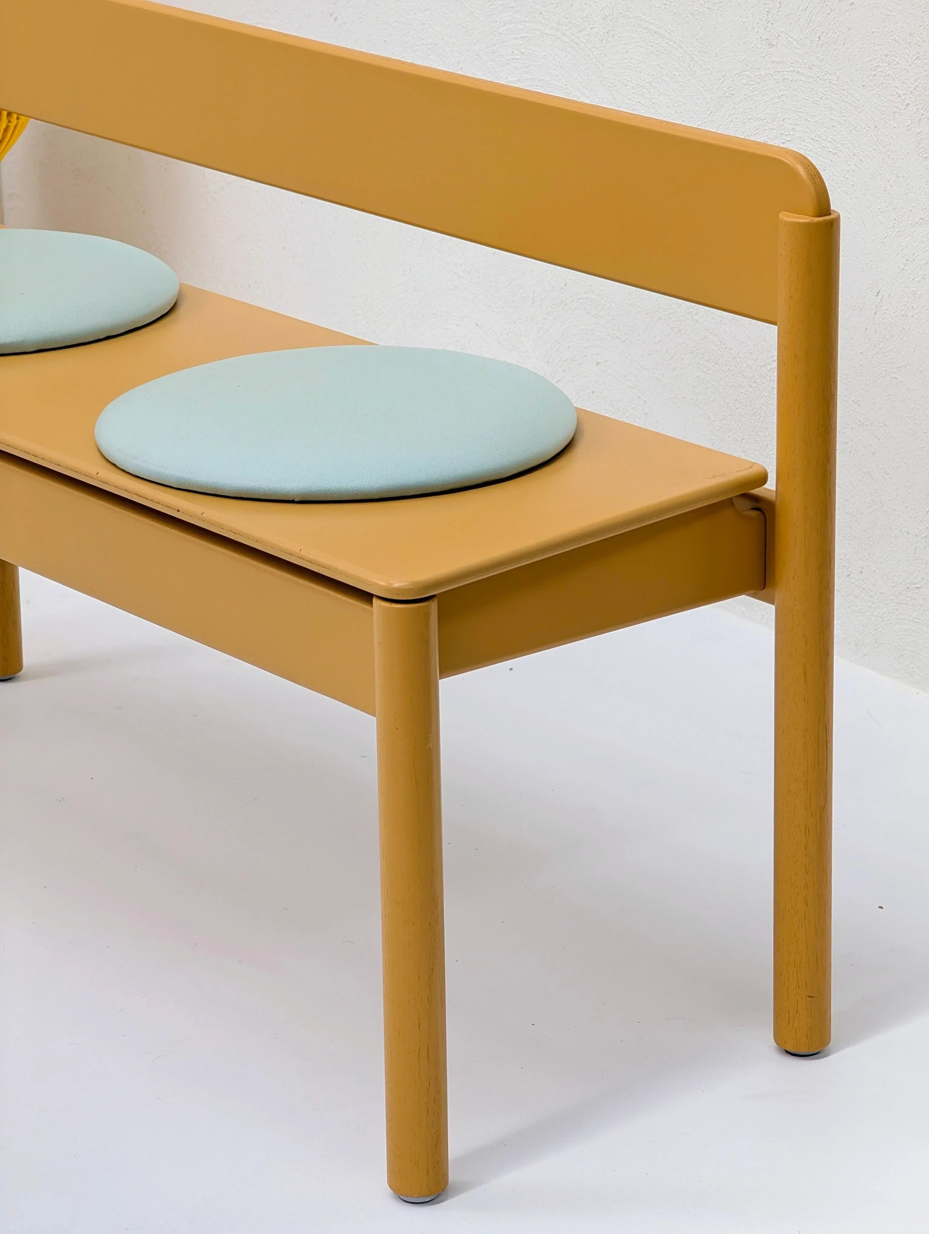 Modern yellow wooden bench with mint green round seat cushions against white background