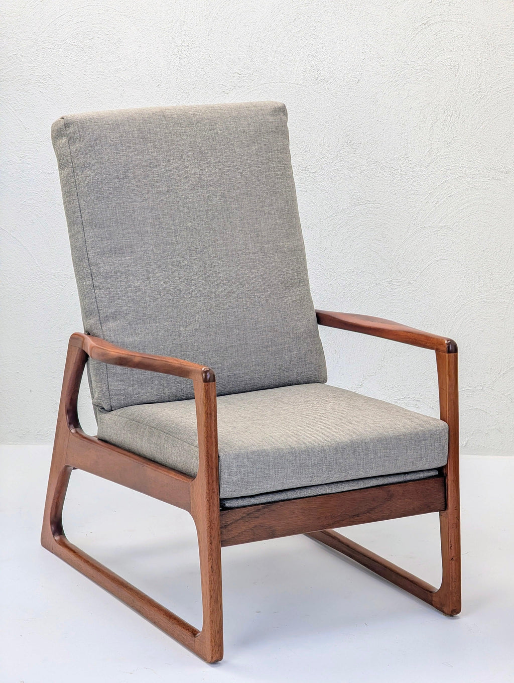 Mid-century modern armchair with grey fabric cushion and walnut wood frame on white background.