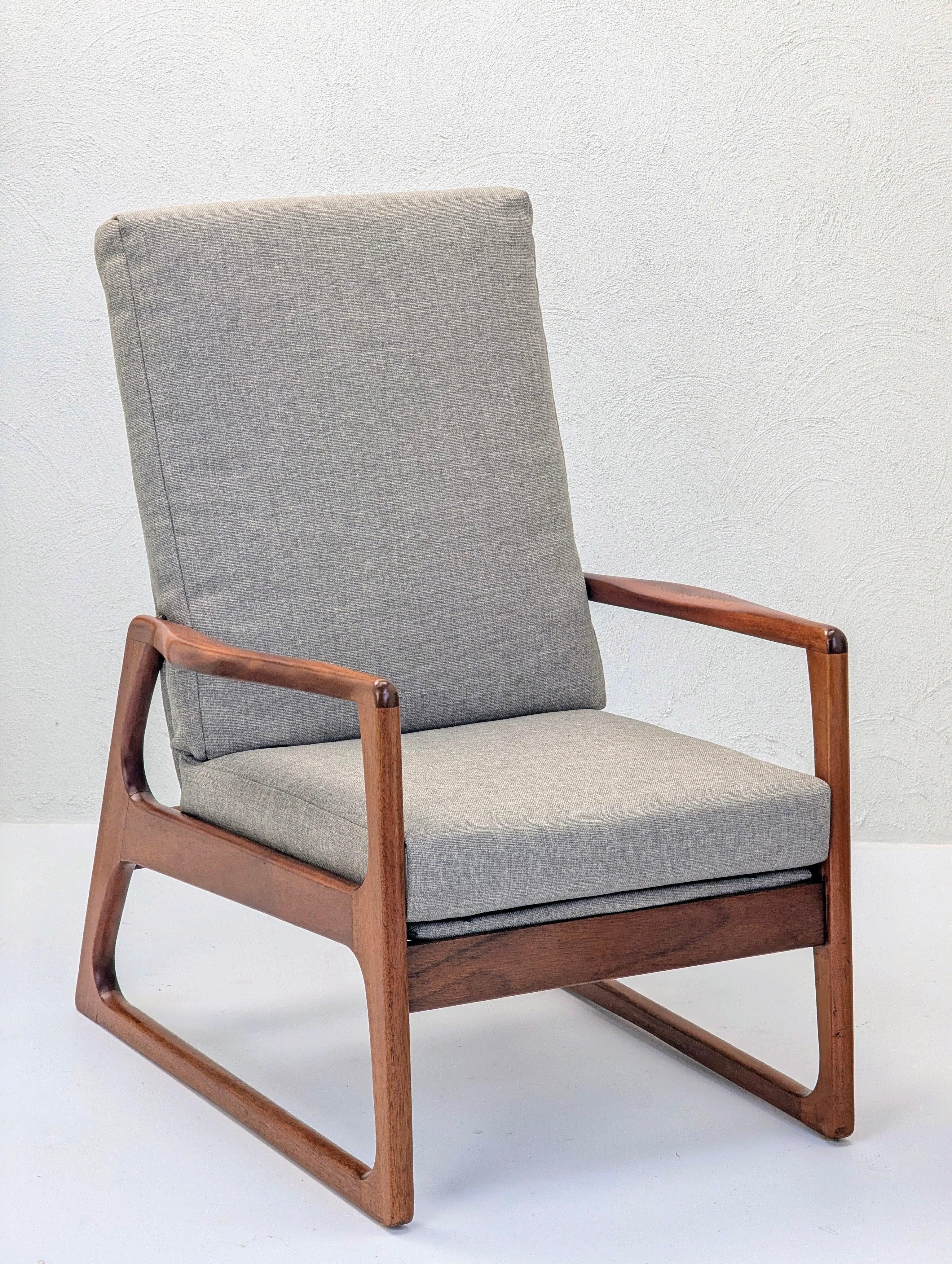 Mid-century modern armchair with grey fabric cushion and walnut wood frame on white background.