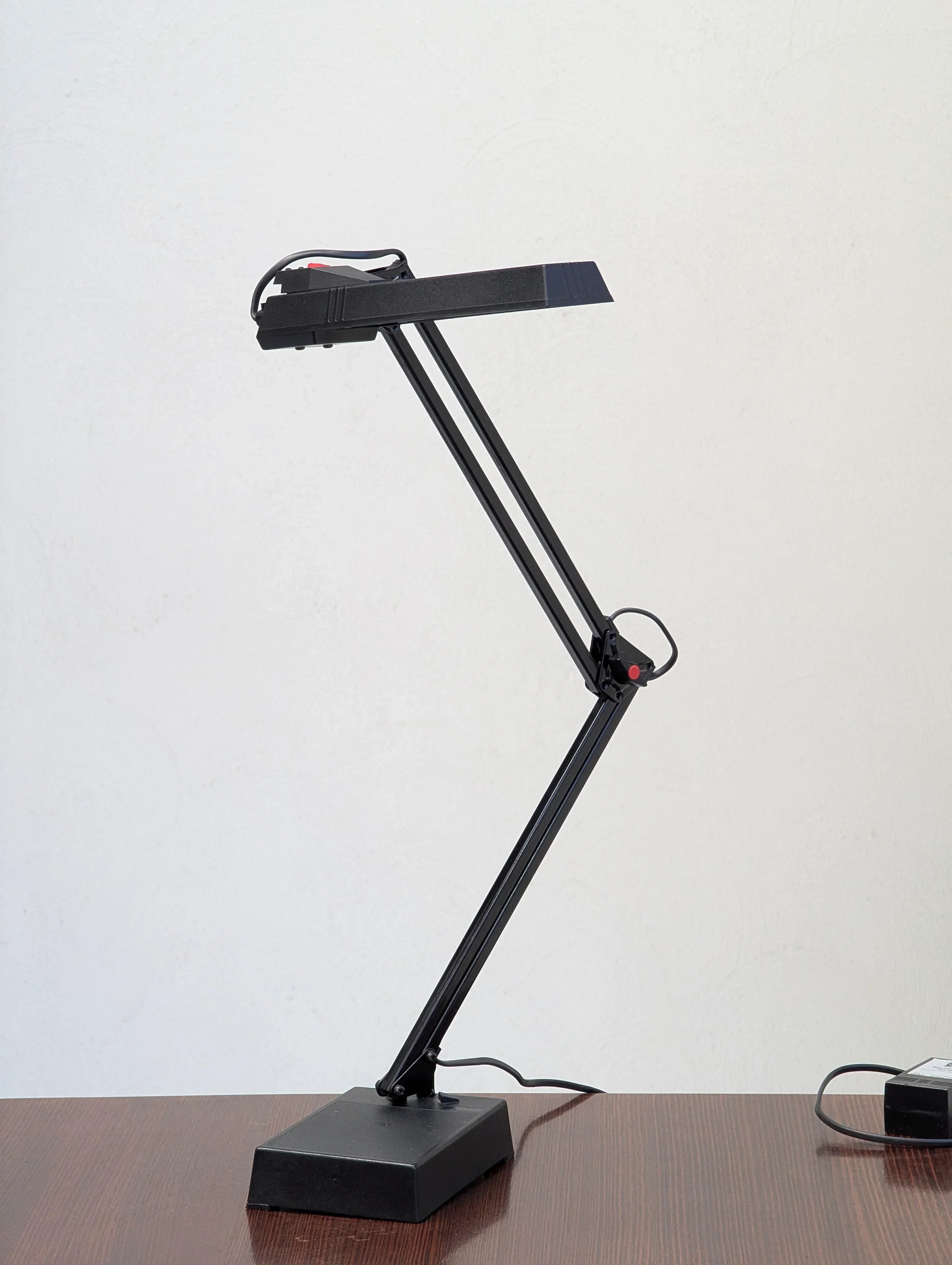 Black adjustable desk lamp on wooden table against plain white wall
