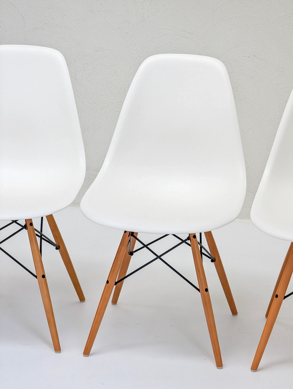 Modern white plastic chairs with wooden legs set against a minimalist white background