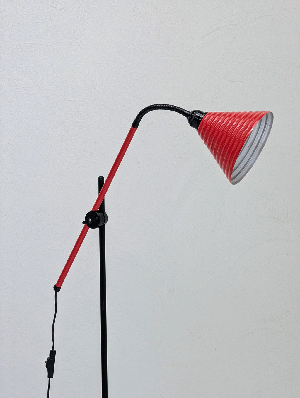 Adjustable red and black floor lamp with conical shade against a white wall