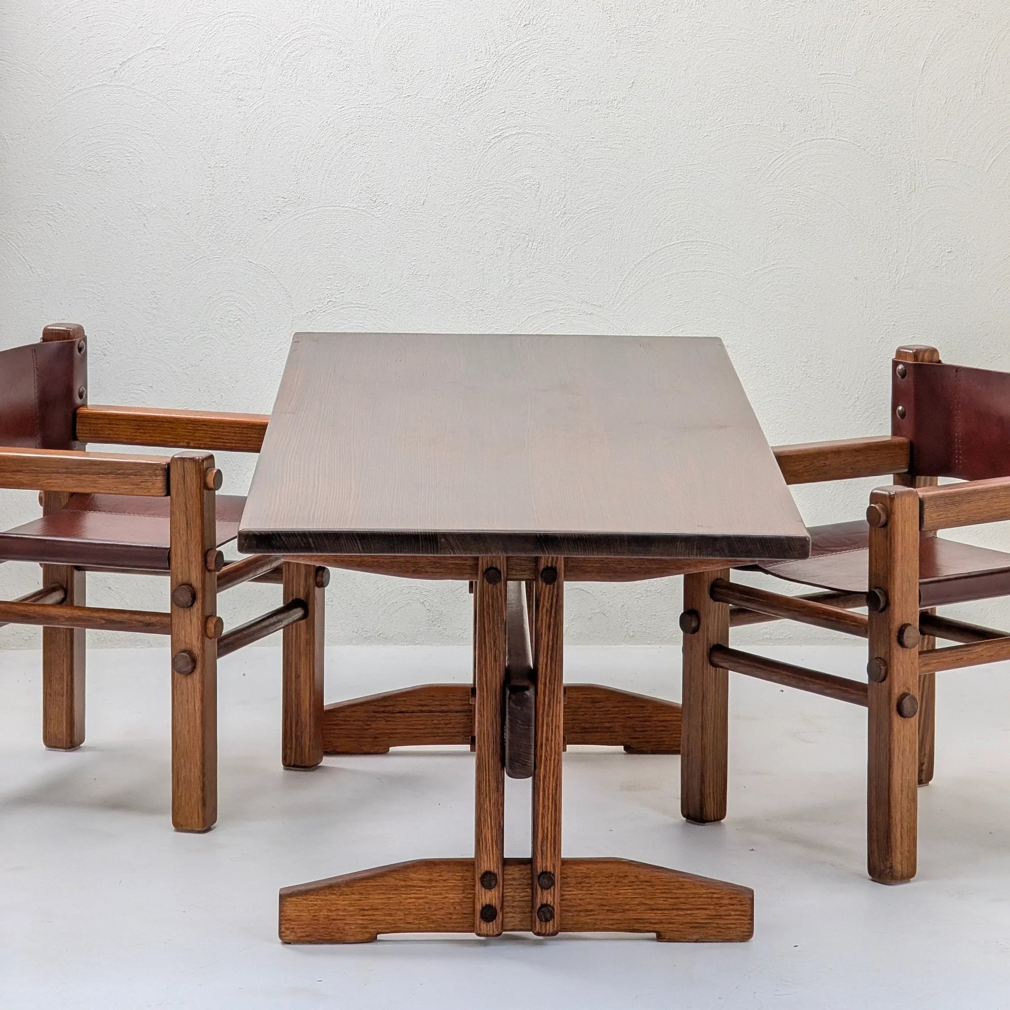 Mid-century modern wood dining table and two matching armchairs against a white wall