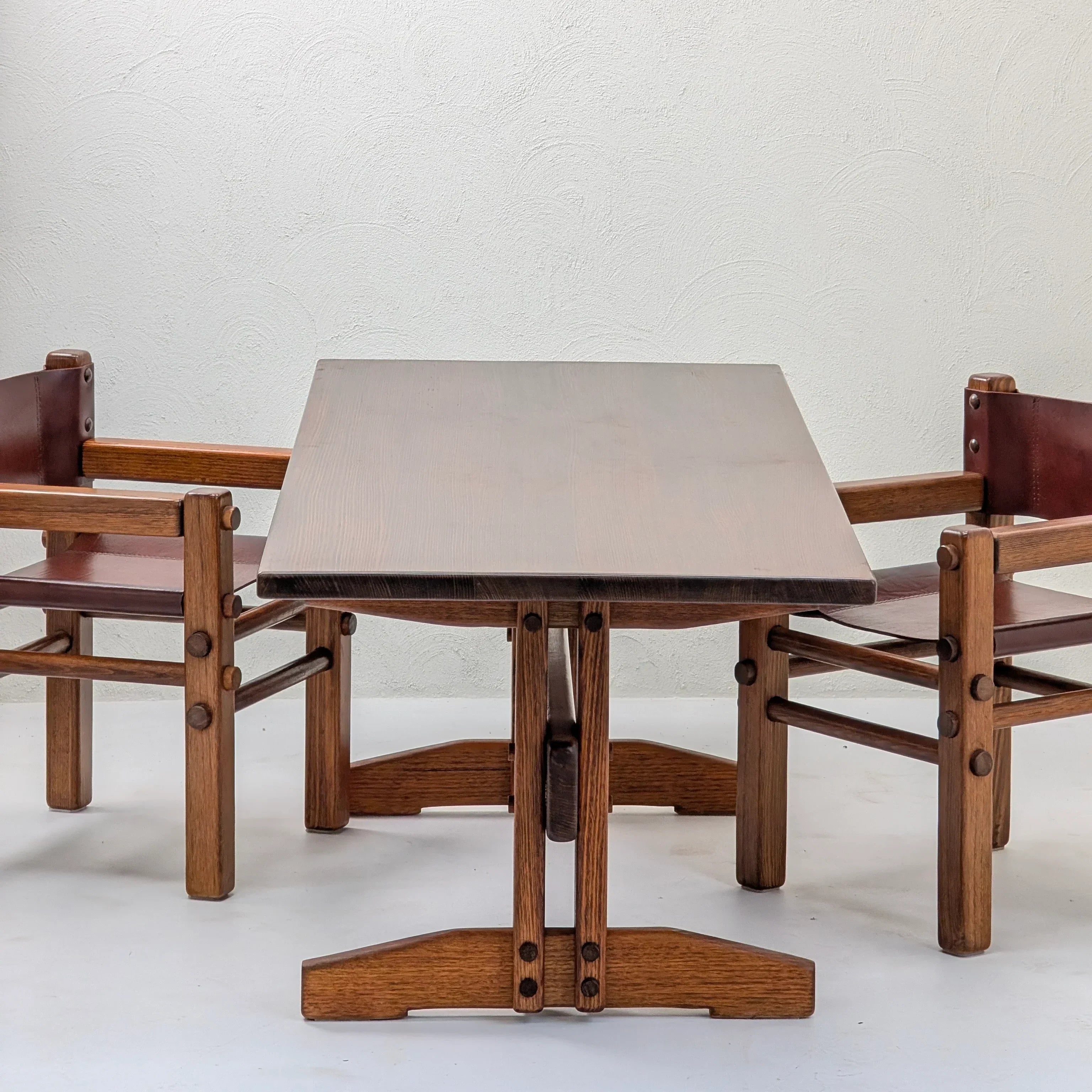 Mid-century modern wood dining table and two matching armchairs against a white wall