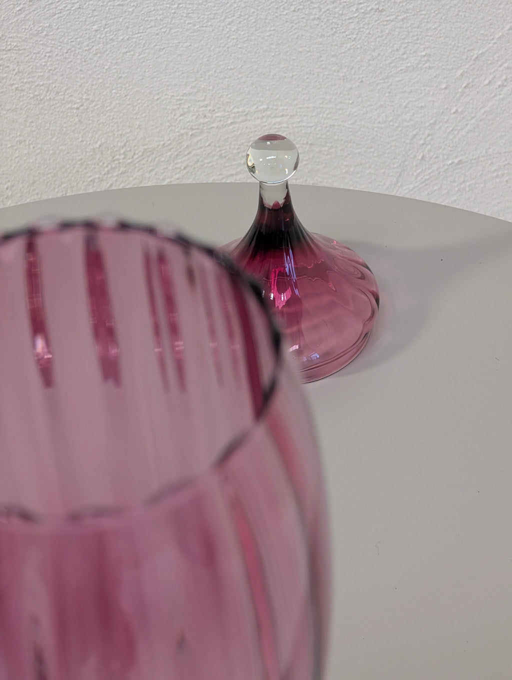 Close-up of pink ribbed glassware with a matching pink glass lid on a white surface