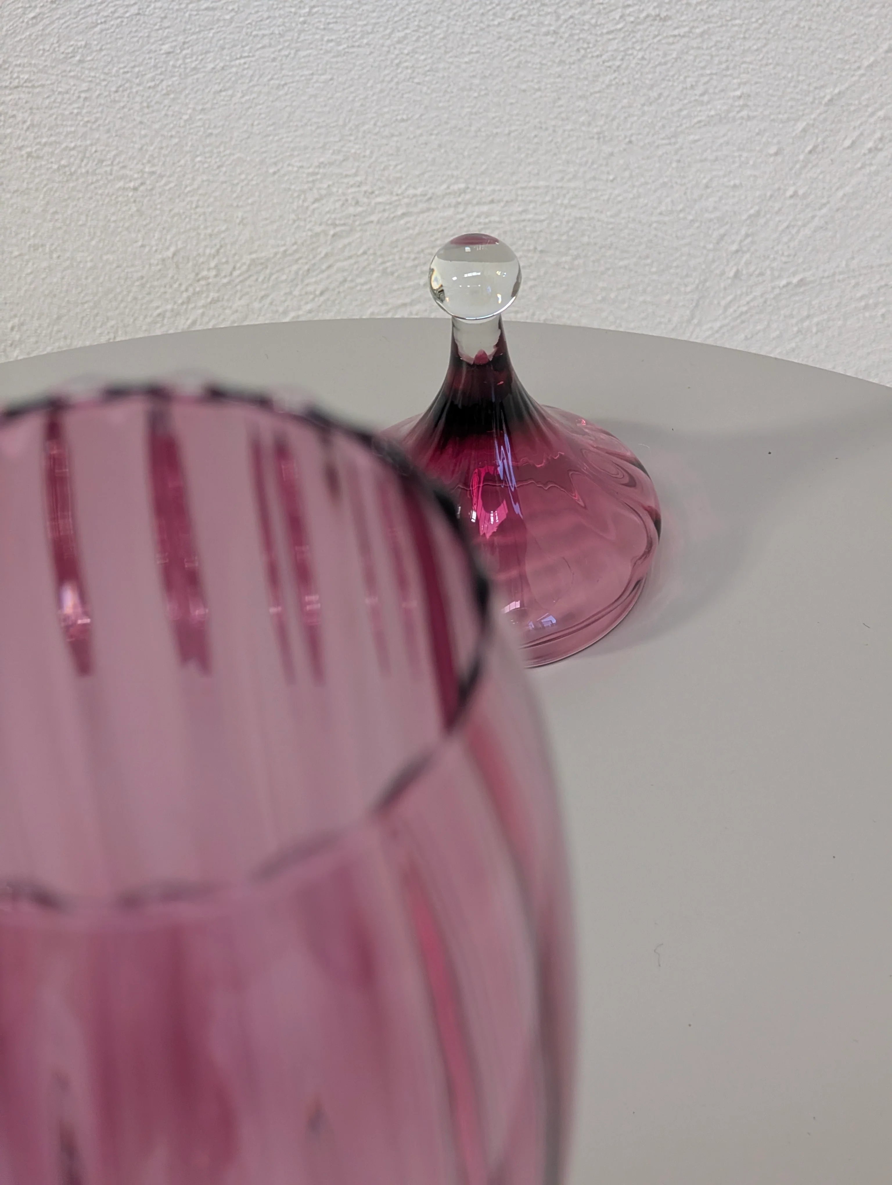 Close-up of pink ribbed glassware with a matching pink glass lid on a white surface