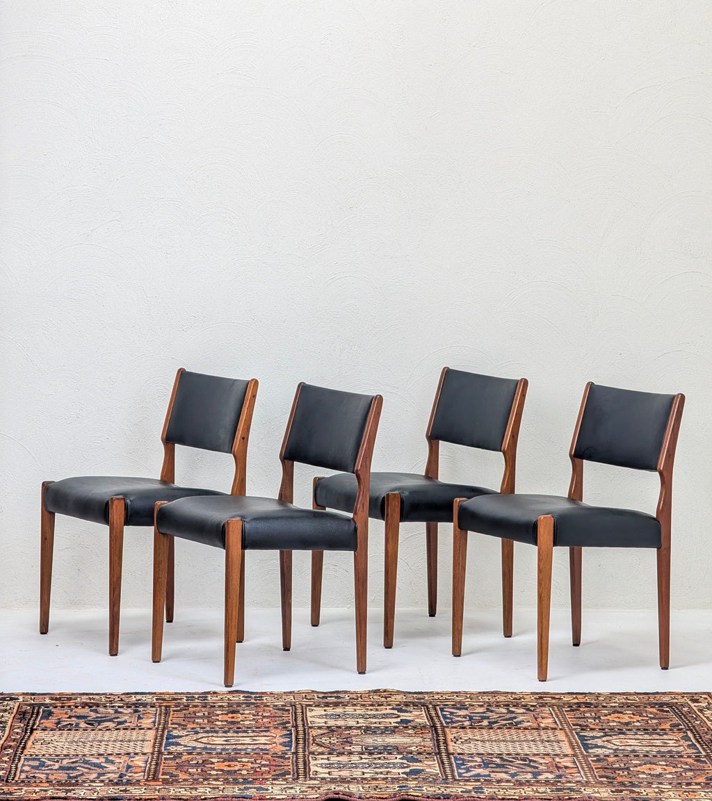 Set of four mid-century modern wooden dining chairs with black leather seats on patterned rug
