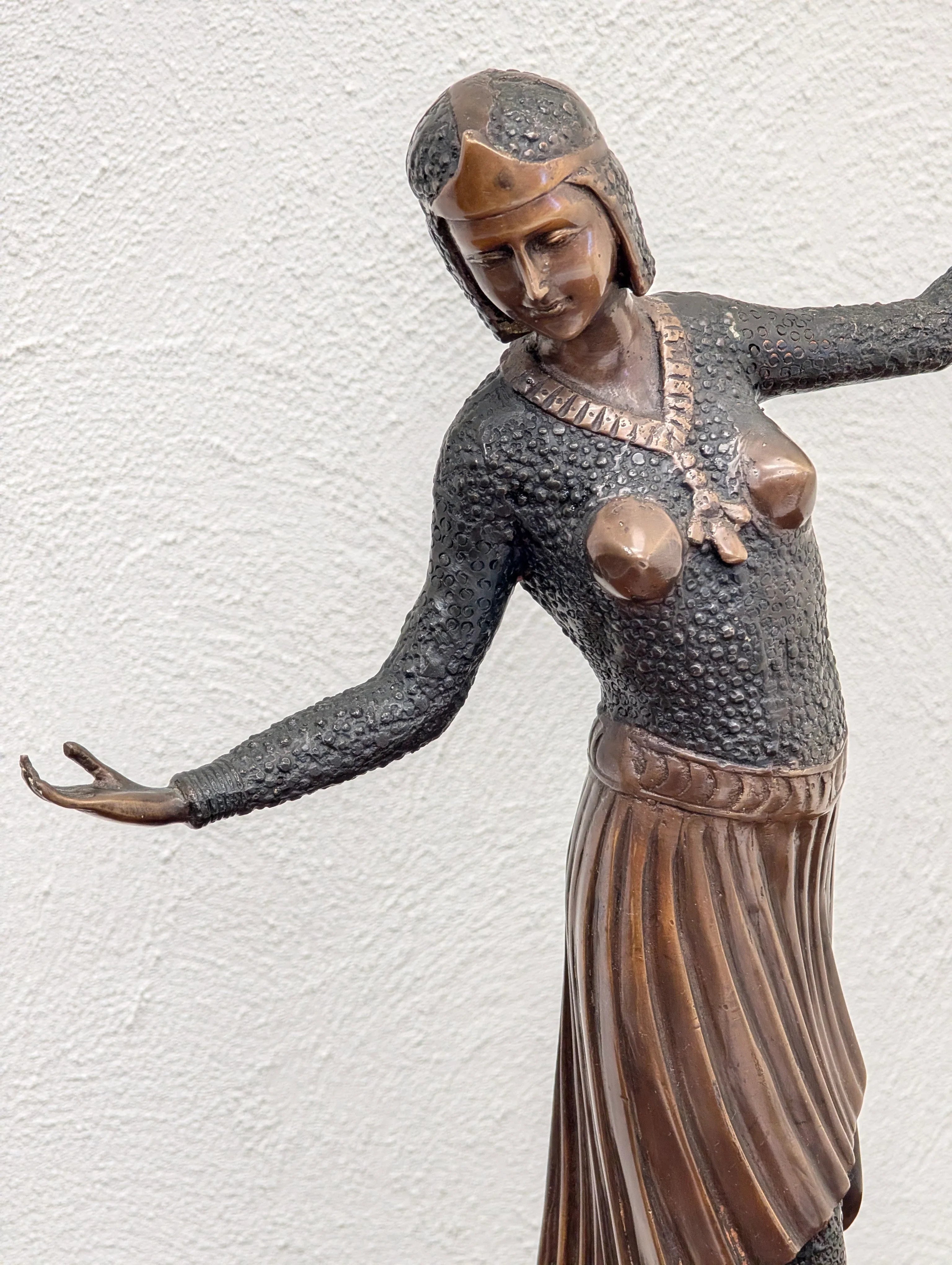 Bronze sculpture of a woman with outstretched arms wearing textured attire and pleated skirt against white background