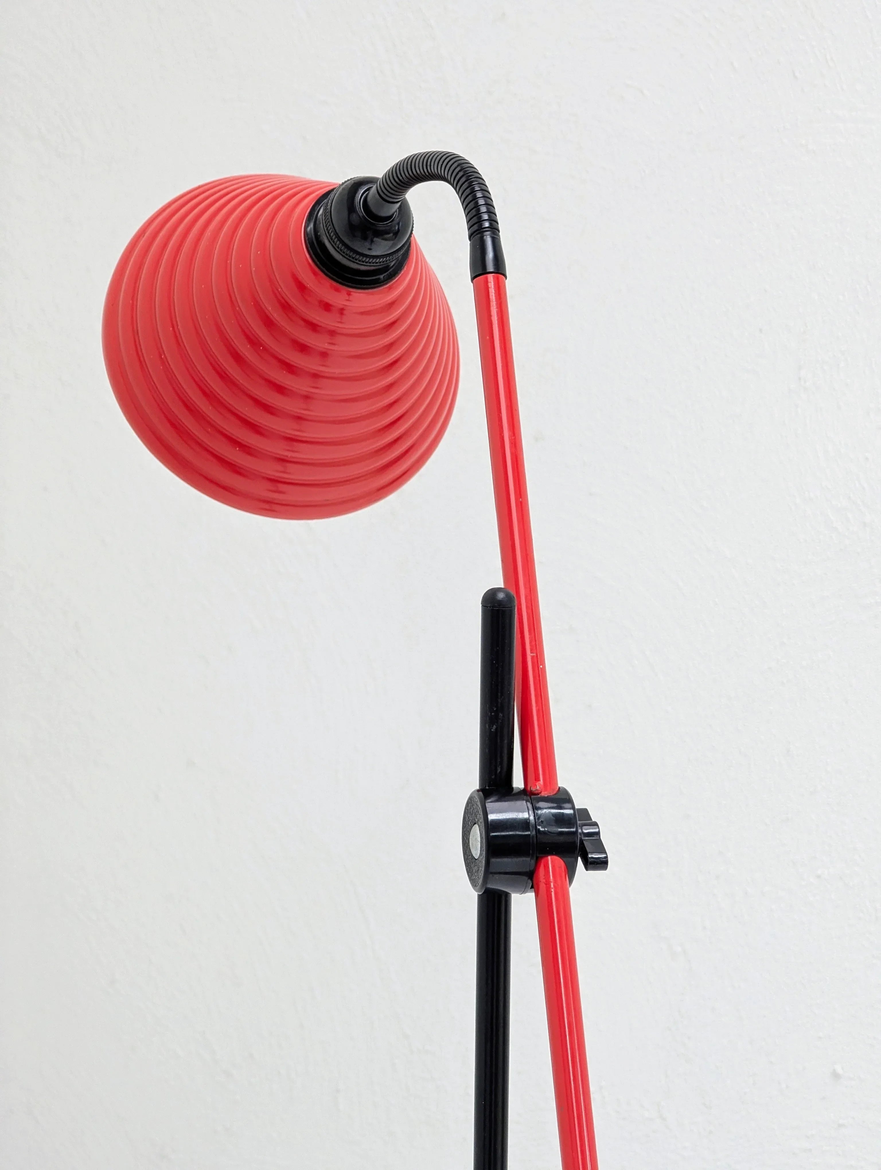 Modern red and black adjustable desk lamp with ribbed shade against white wall