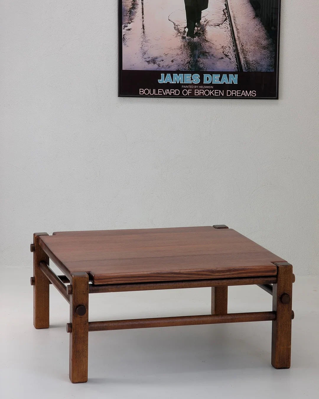 Minimalist wooden coffee table with sturdy frame and plank top against white wall with James Dean poster