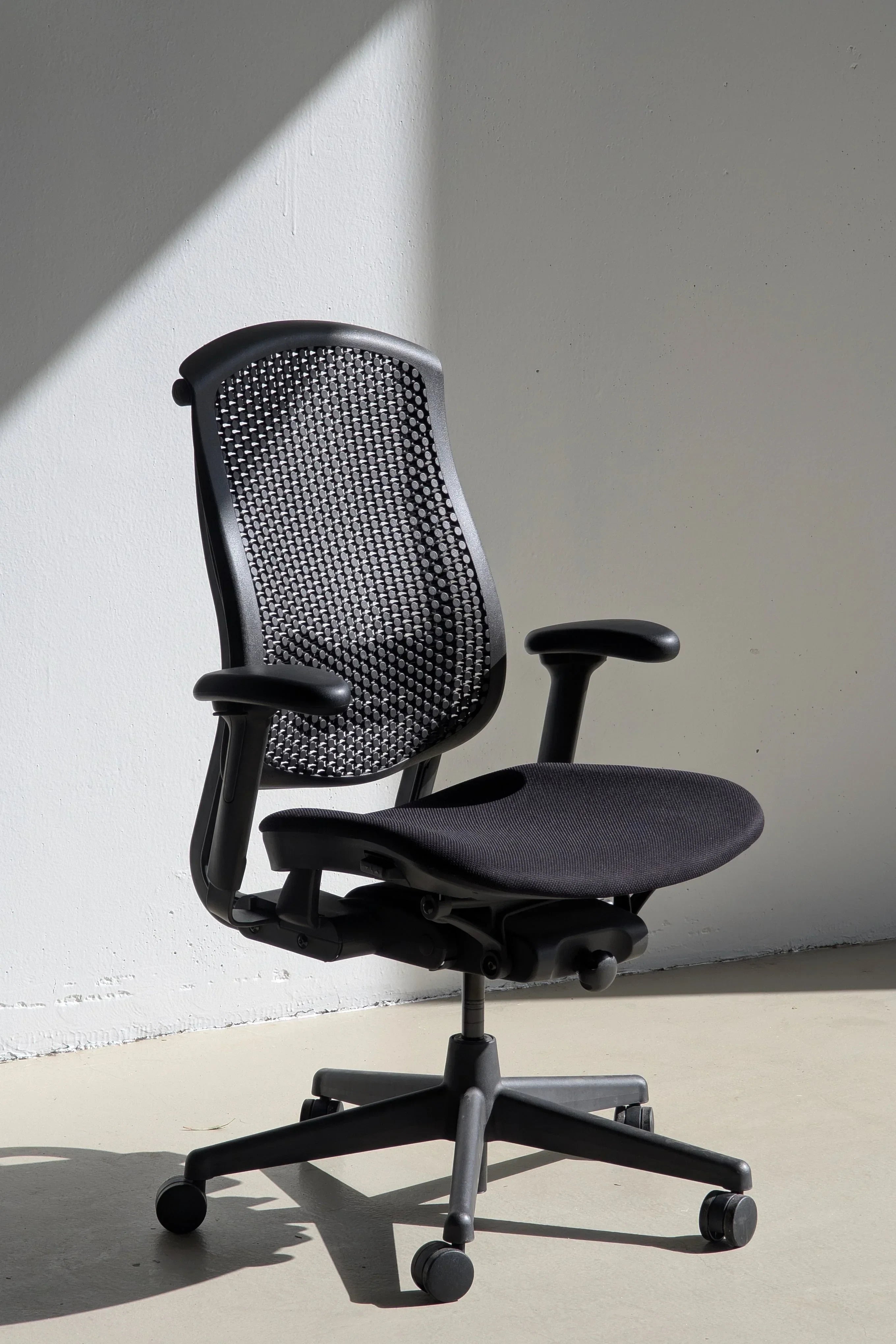 Ergonomic black mesh office chair with armrests on wheels in minimalist room