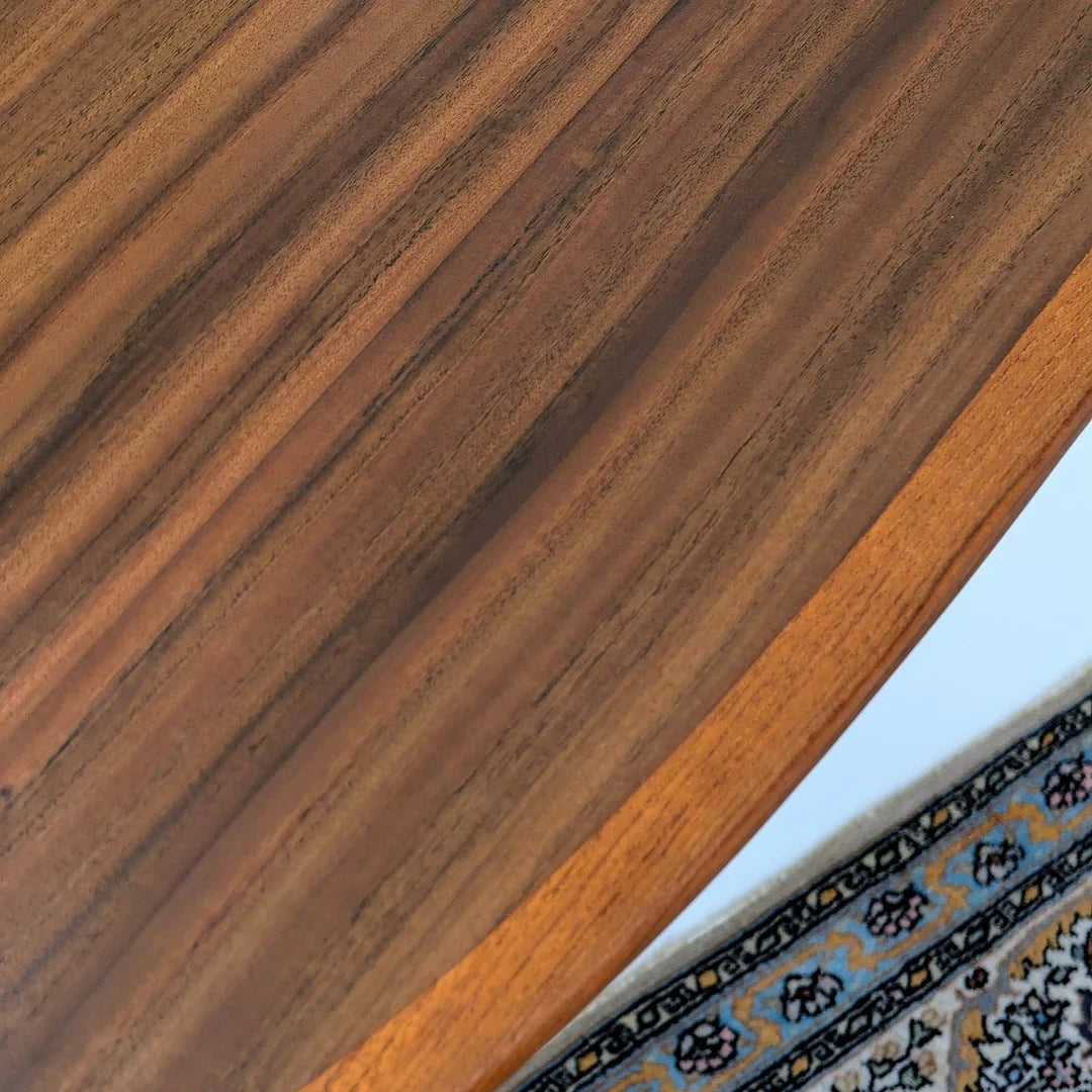 Close-up of a walnut wood table edge beside a patterned area rug
